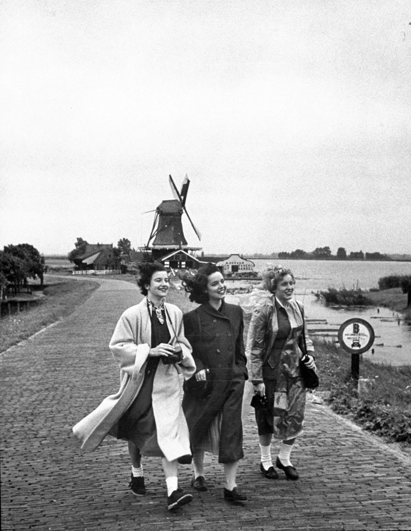 Girls walk away from a Dutch windmill after photographing it.