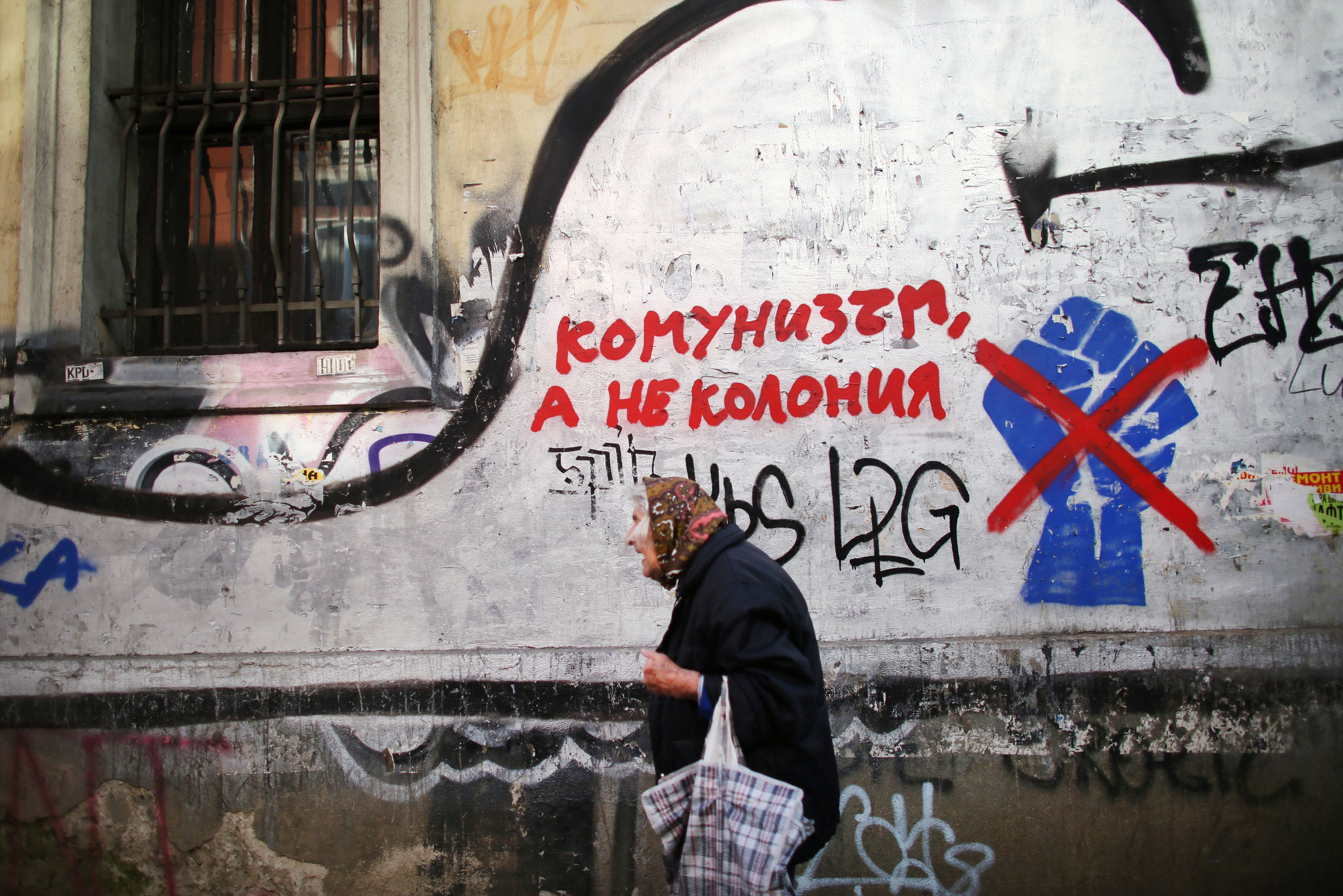 A woman walks by graffiti of a fist in Sofia, the capital of Bulgaria, Oct. 4, 2014. The fist came to symbolize civic protests against political corruption in 2013. It has been crossed off by a second layer of graffiti, with an adjacent sign that reads, 'Communism, but not a Colony,' in likely reference to what some political parties decry as Westernization of interests in the country.