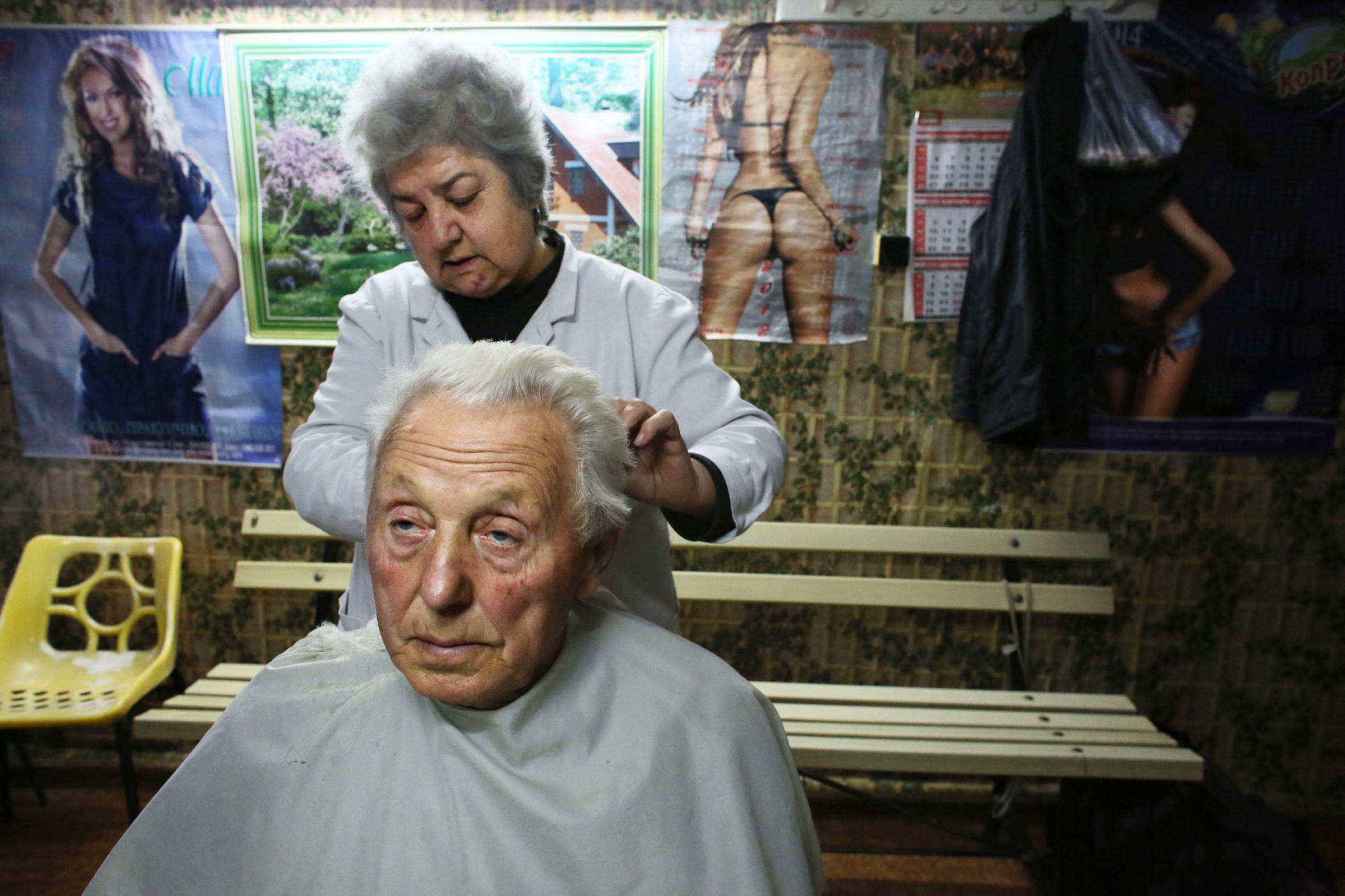 Hair dresser Pavlinka Paskova, 59, cuts the hair of Stanko Petrov Vulchev, 80, in Vidin, Bulgaria, on October 30th, 2014. Paskova says she has very few customers in this town of waning population: "There's little hope of prosperity for the young here - they've all emigrated."Bulgaria has the most extreme population decline in the world ó much due to post-1989 emigration, high death rates and low birth rates. There are so few people of child-bearing age in the nation that population statistics project a 30-percent decrease by 2060, from 7.2 million to just over 5 million. In other words,†Bulgariaís population declines by 164 people a day, or 60,000 people a year ó 60 percent of them aged over 65.This photo is from a project that aims to gauge the state and effect of democracy in the former Soviet satellite nation Bulgaria, two and a half decades after the fall of the Berlin Wall. The story of democracy in Bulgaria at age 25 is a cautionary tale about transplanting one-size-fits-all Western values to a nation still undergoing social and economic upheaval. Bulgaria is still one of the poorest, most corrupt nations in the European Union, its post-1989 hopes wilted by political instability, high crime rates and skyrocketing inflation. While Bulgarians can now freely vote and protest without much threat to their freedom, their new oppressor is corruption - which is at a 15 year high, across political and civil sectors alike. The ennui is so casually etched on the passerby's face that it becomes routine - one that fits in sadly well against a startling backdrop of rotting architecture, joblessness, and a vast population decline. Despite what democracy has changed in Bulgaria, the daily struggles of its populace remain largely untouched, trapped in a post-communist time capsule.This project was supported by a grant from The Pulitzer Center on Crisis Reporting. Photo by: Yana PaskovaCopyright © Yana Paskova 2014