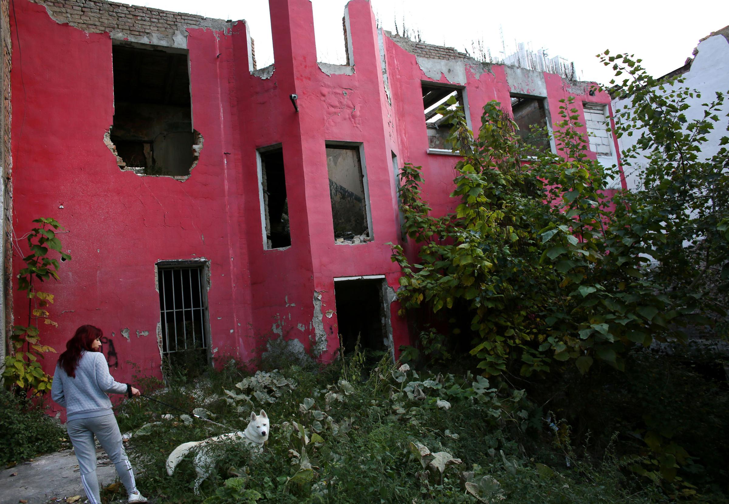 A woman walks her dog by an abandoned building in Vidin, a town of rapidly declining population in Western Bulgaria, on October 22nd, 2014. Bulgaria has the most extreme population decline in the world ó much due to post-1989 emigration, high death rates and low birth rates. There are so few people of child-bearing age in the nation that population statistics project a 30-percent decrease by 2060, from 7.2 million to just over 5 million. In other words,†Bulgariaís population declines by 164 people a day, or 60,000 people a year ó 60 percent of them aged over 65.This photo is from a project that aims to gauge the state and effect of democracy in the former Soviet satellite nation Bulgaria, two and a half decades after the fall of the Berlin Wall. The story of democracy in Bulgaria at age 25 is a cautionary tale about transplanting one-size-fits-all Western values to a nation still undergoing social and economic upheaval. Bulgaria is still one of the poorest, most corrupt nations in the European Union, its post-1989 hopes wilted by political instability, high crime rates and skyrocketing inflation. While Bulgarians can now freely vote and protest without much threat to their freedom, their new oppressor is corruption - which is at a 15 year high, across political and civil sectors alike. The ennui is so casually etched on the passerby's face that it becomes routine - one that fits in sadly well against a startling backdrop of rotting architecture, joblessness, and a vast population decline. Despite what democracy has changed in Bulgaria, the daily struggles of its populace remain largely untouched, trapped in a post-communist time capsule.This project was supported by a grant from The Pulitzer Center on Crisis Reporting. Photo by: Yana PaskovaCopyright © Yana Paskova 2014