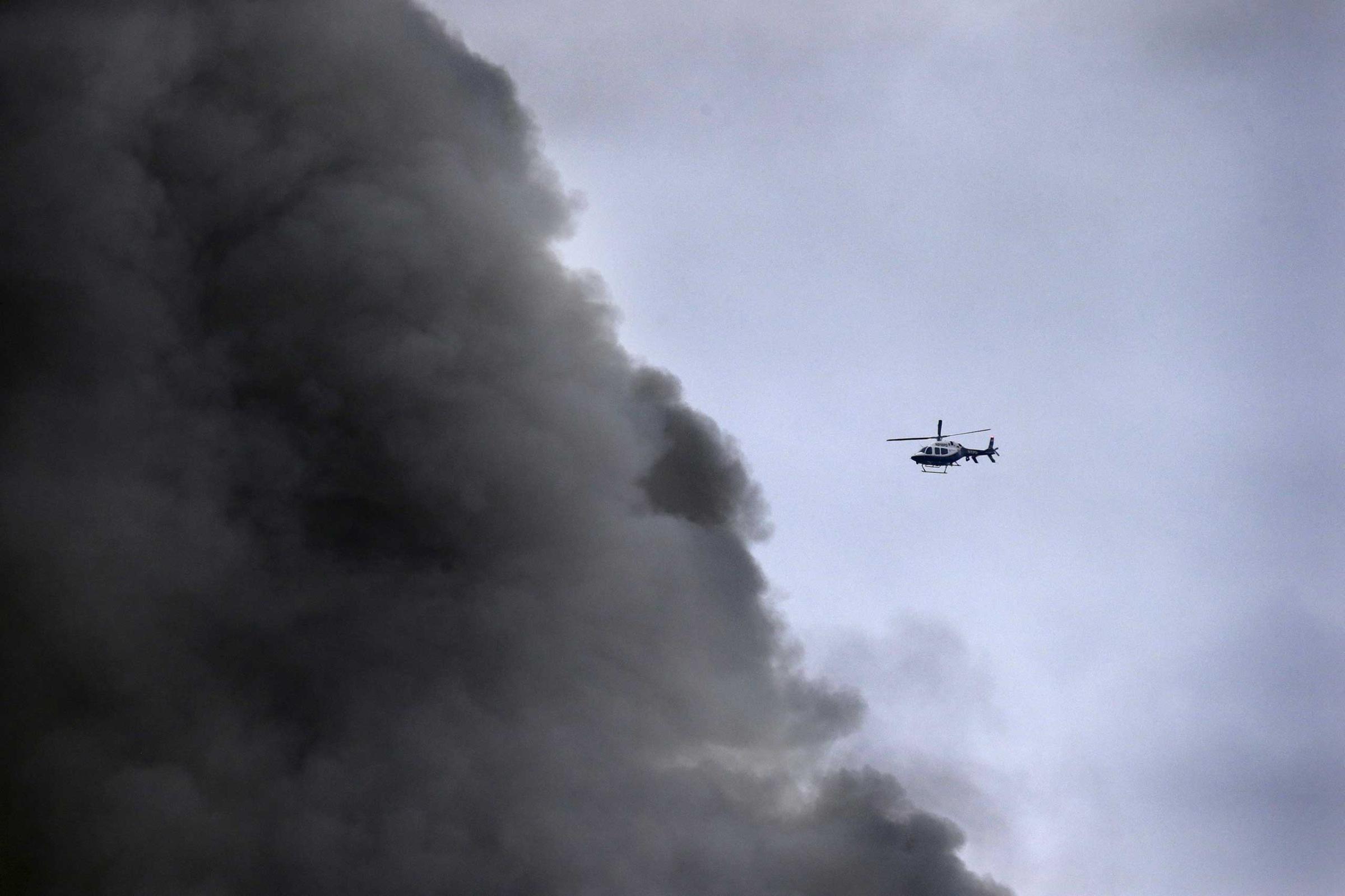 A New York City Police helicopter flies near billowing smoke above the site of a residential apartment building collapse and fire in New York City's East Village neighborhood