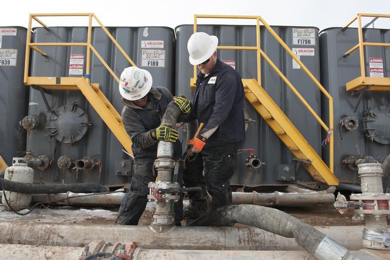 Mody Torres (L) and Josh Anderson of Select Energy Services connect hoses between a pipeline and water tanks at a Hess fracking site near Williston, North Dakota Nov. 12, 2014.