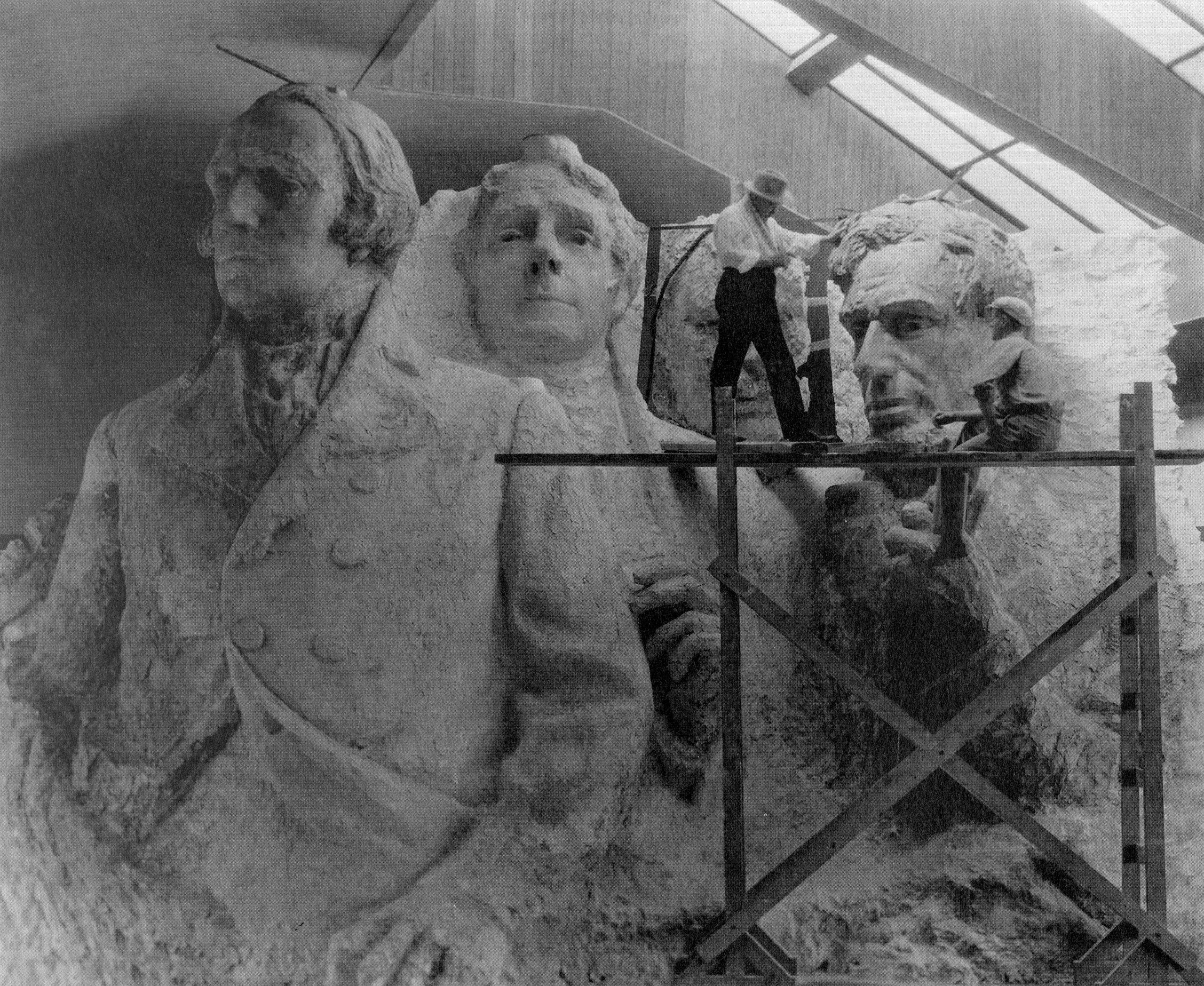 The sculptor of Mount Rushmore, Gutzon Borglum, with a model of the four presidents that included arms and hands.