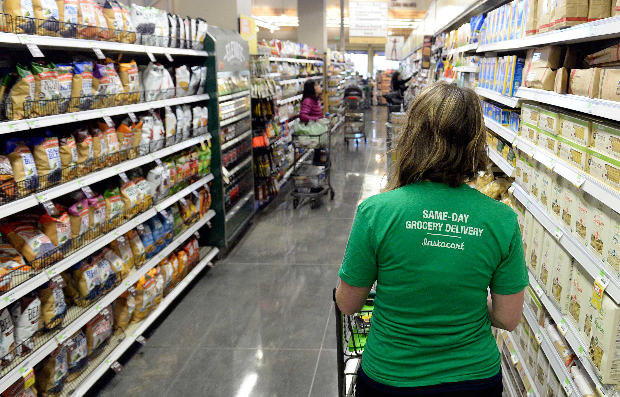 Kaitlin Myers a shopper for Instacart studies her smart phone as she  shops for a customer at Whole Foods in Denver.