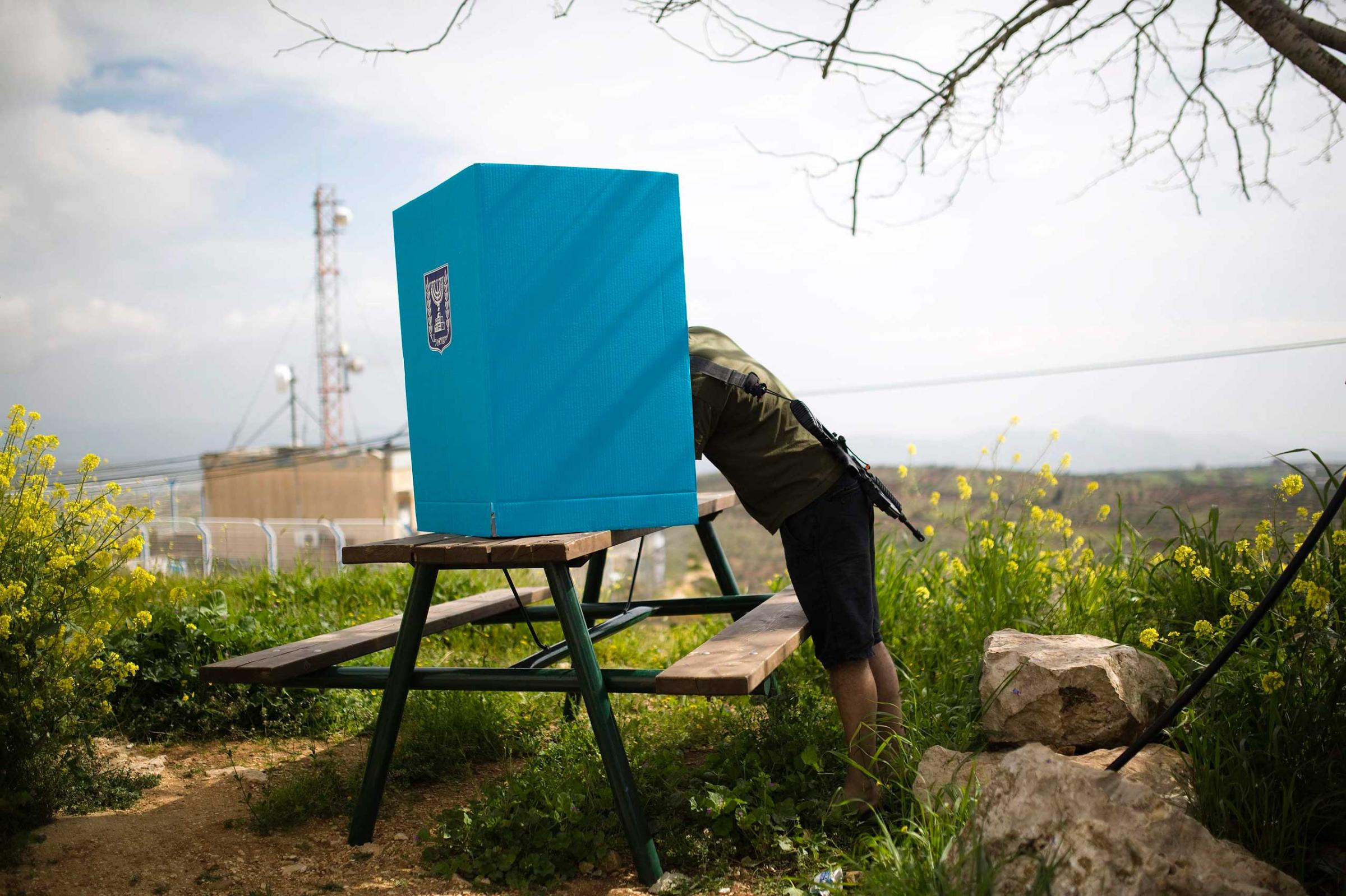 An Israeli soldier casts his ballot for the parliamentary election behind a mobile voting booth in the West Bank Jewish settlement of Migdalim, near Ariel, March 17, 2015.