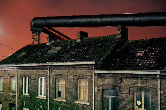 The gas supply tubes run along the houses built near the steel factories of Charleroi. Before the electric upgrade of the blast furnace these tubes used to provide the energy necessary to this operation. The factory and furnace infringe and loom over the lives of the inhabitants.