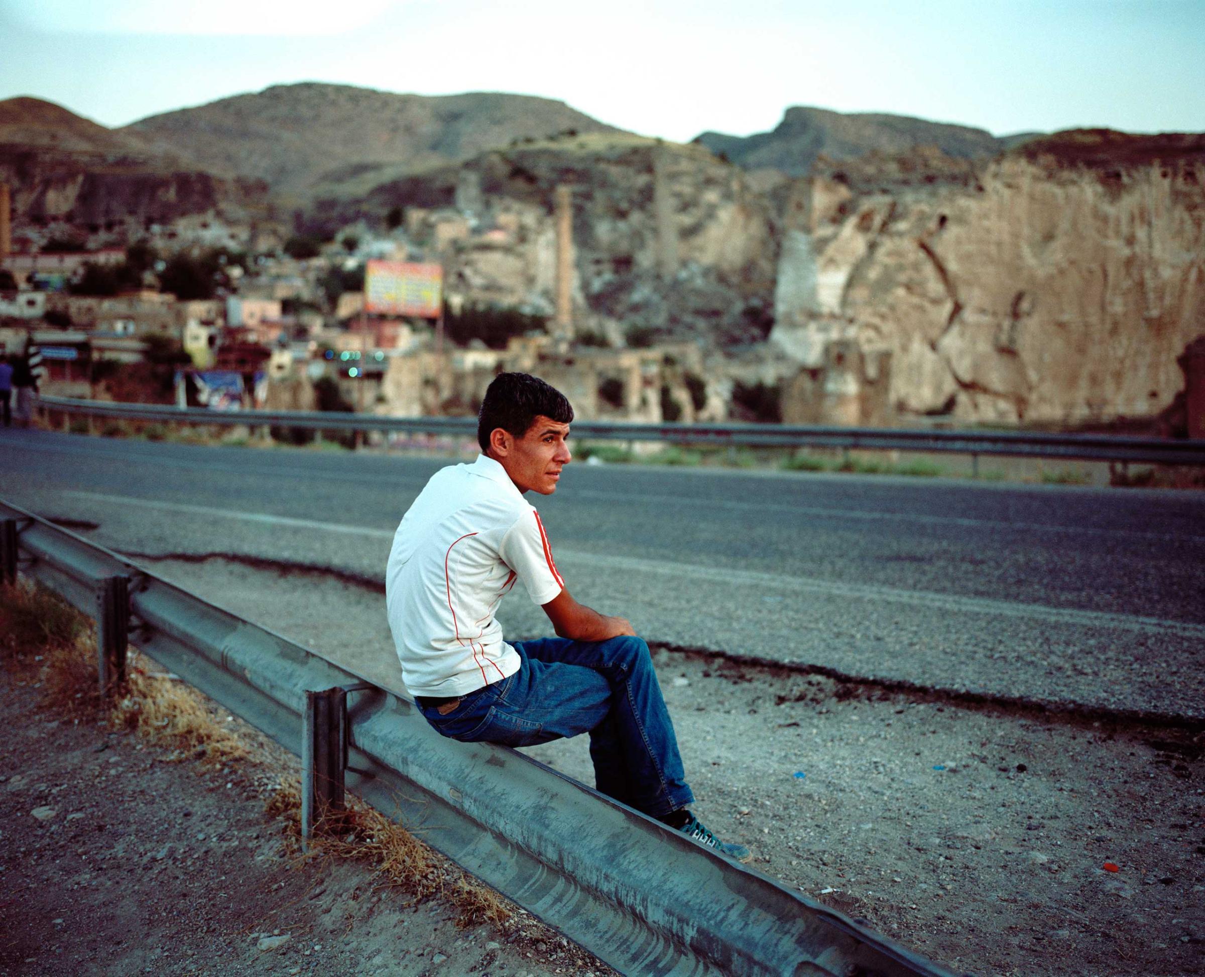 A man sits by the road along the bridge leading to Hasankeyf over the Tigris River. Hasankeyf, Turkey.