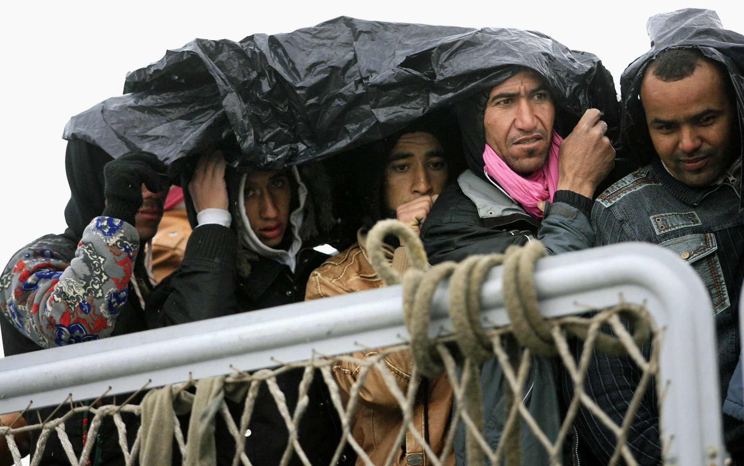 Migrants protect themselves from the rain as they wait to disembark from a ship on Feb. 17, 2015 in Porto Empedocle, south Sicily, following a rescue operation of migrants as part of the International Frontex plan.
