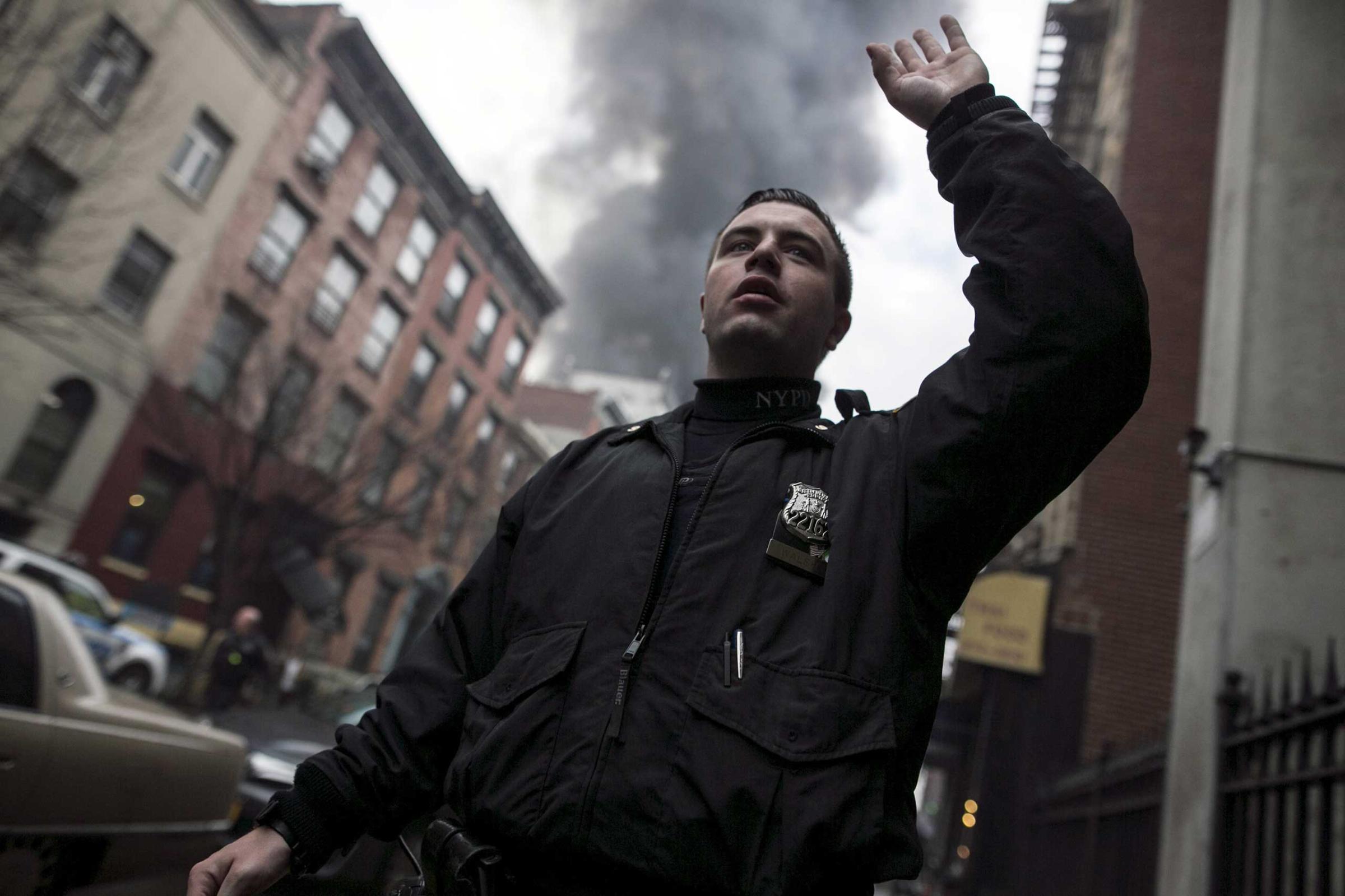 A NYPD signals residents way from the site of a building fire in the East Village neighborhood of New York City