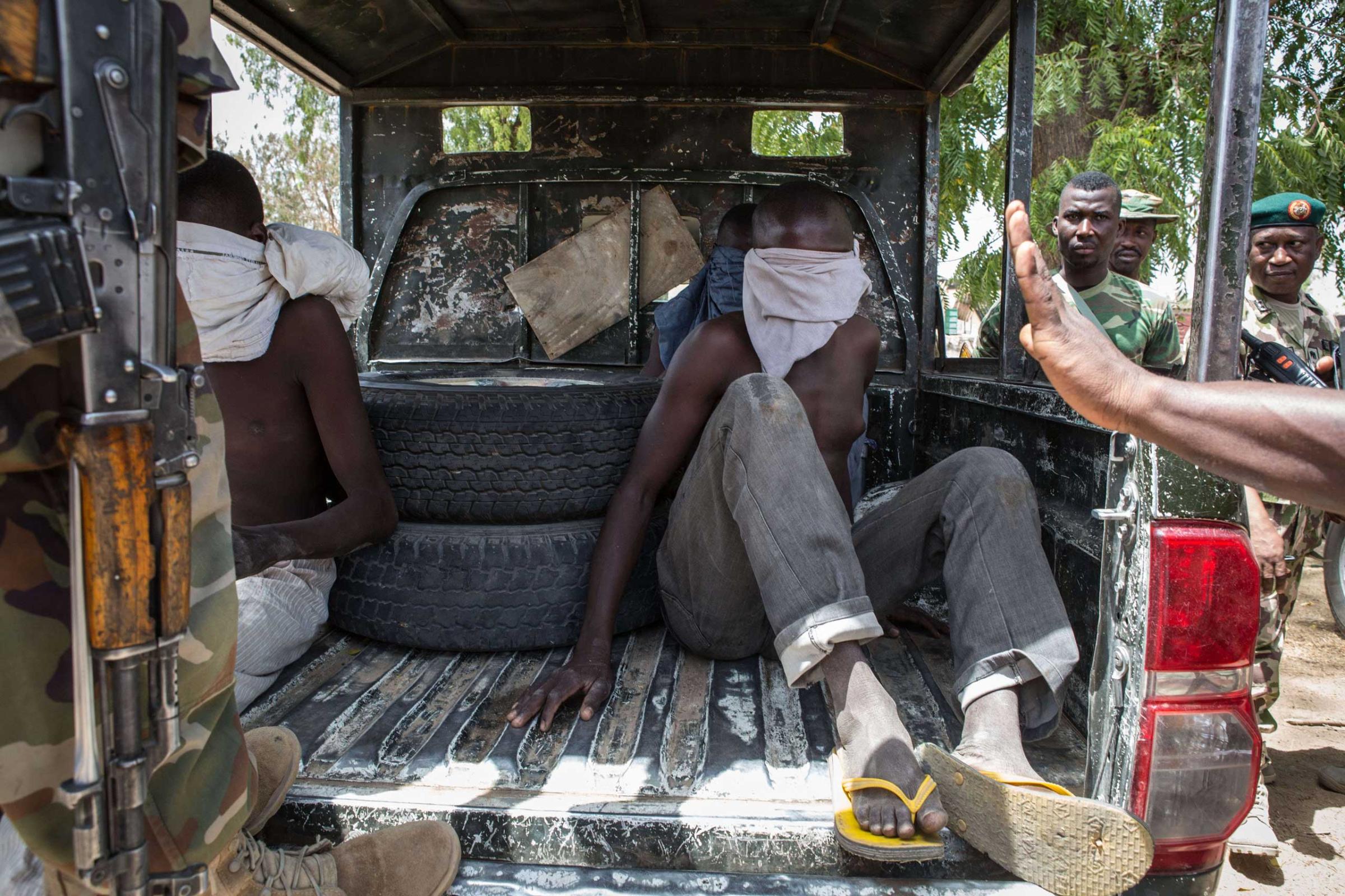 Three young men, who were discovered while entering Bama, sit blindfolded in the back of a pick-up truck before being taken for interrogation by the Nigerian army in Bama on March 25, 2015.