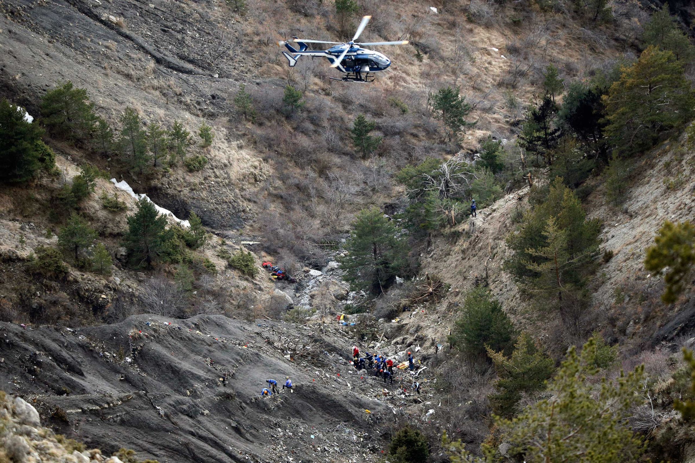 A helicopter flies overhead as rescue workers work at the crash site of Germanwings passenger plane near Seyne-les-Alpes, France, on March 26, 2015.
