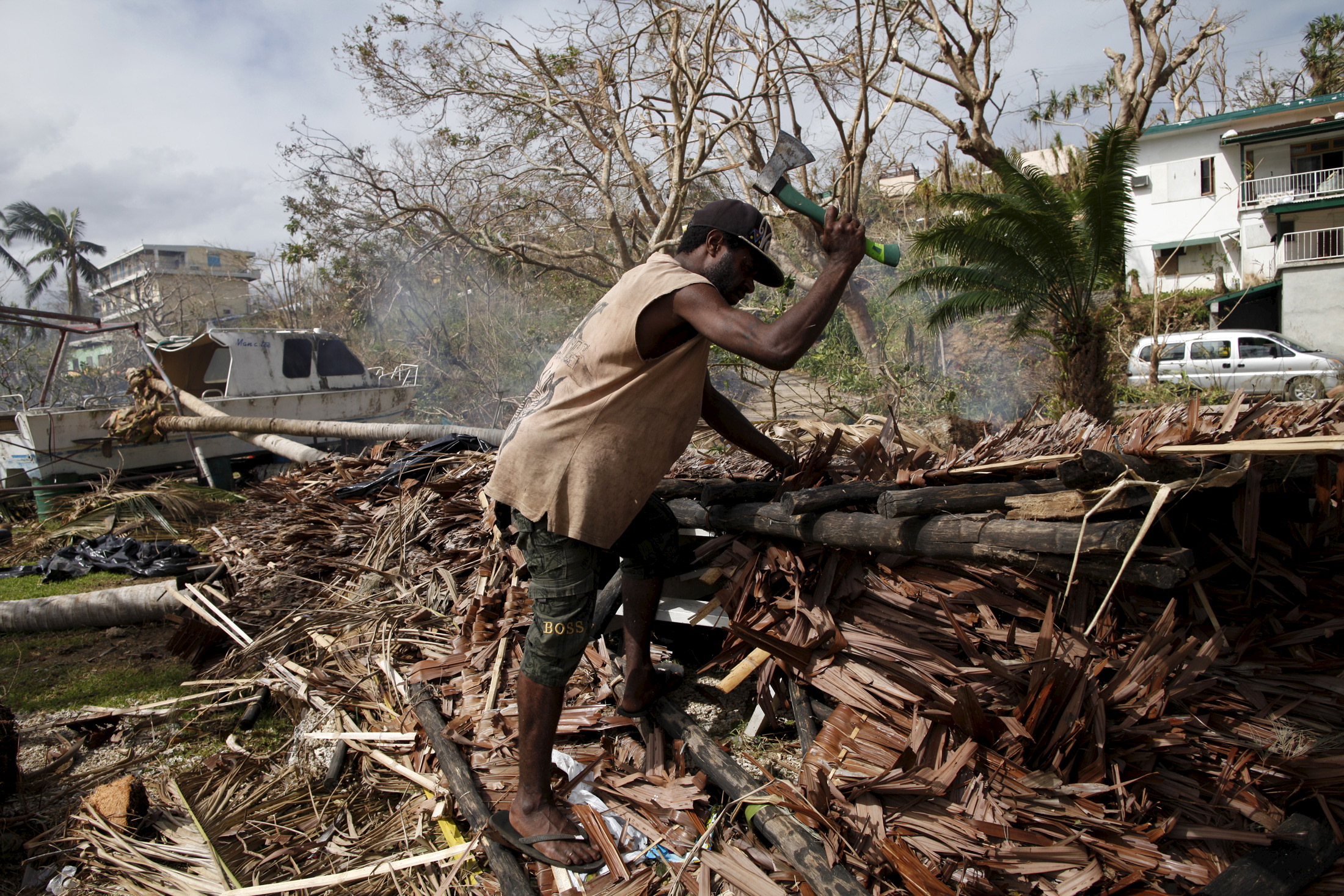 A worker chops up fallen trees next to a destroyed boat at a resident's compound days after Cyclone Pam in Port Vila, capital city of the Pacific island nation of Vanuatu March 19, 2015.