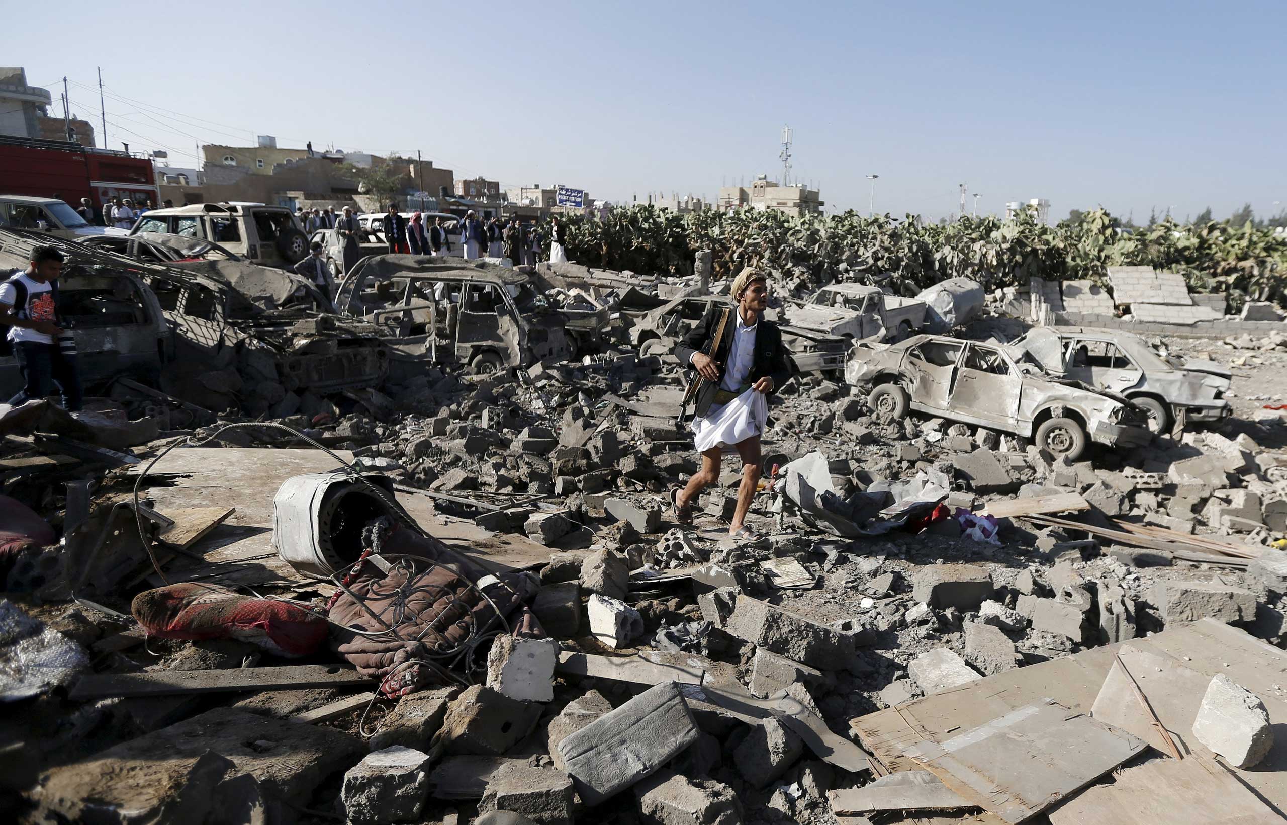 An armed man walks on the rubble of houses destroyed by an air strike near Sanaa Airport