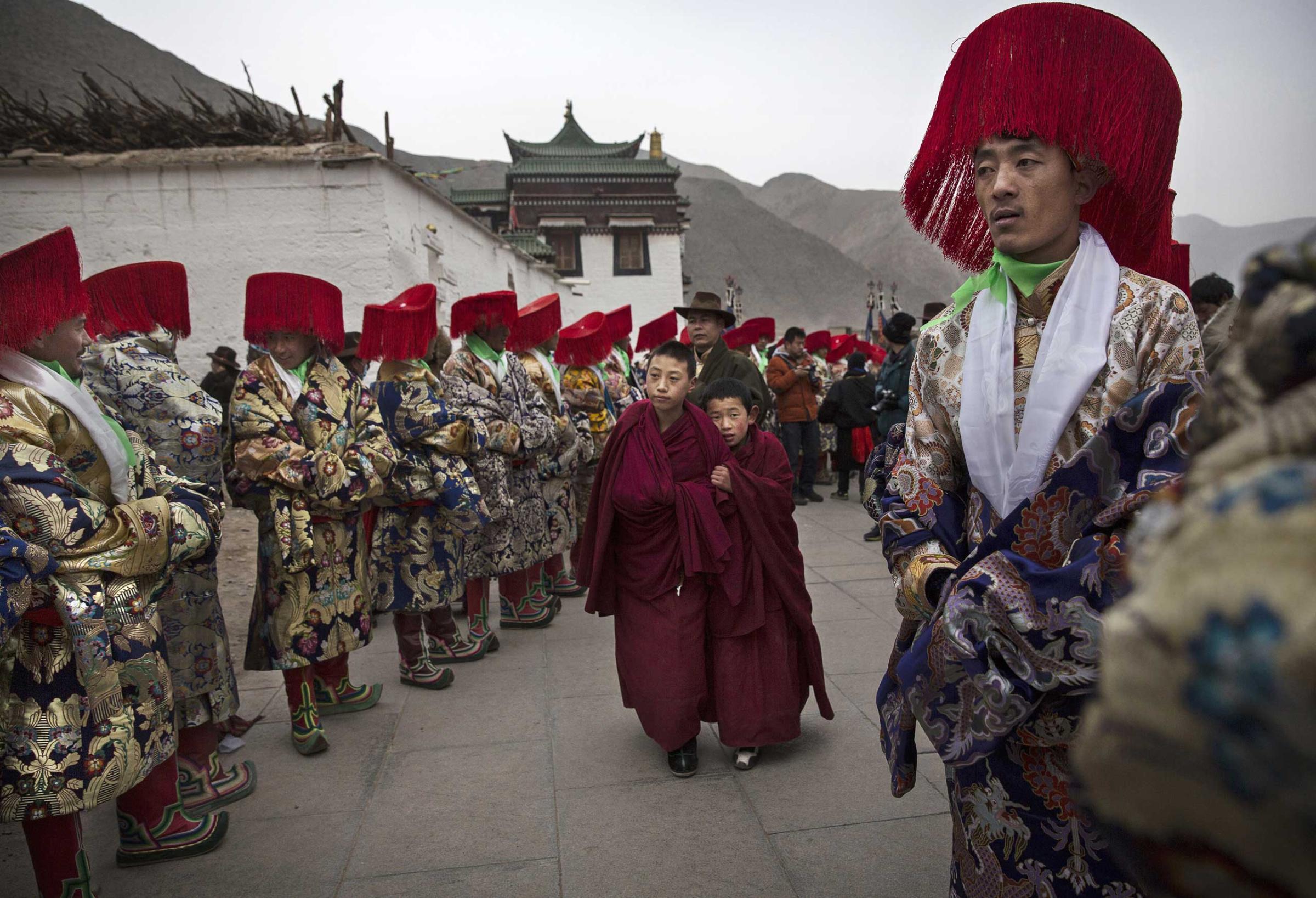 Two young Tibetan Buddhist monks of the Gelug, or Yellow Hat order, walk passed men in traditional clothing before a procession during Monlam or the Great Prayer rituals on March 4, 2015 at the Labrang Monastery.