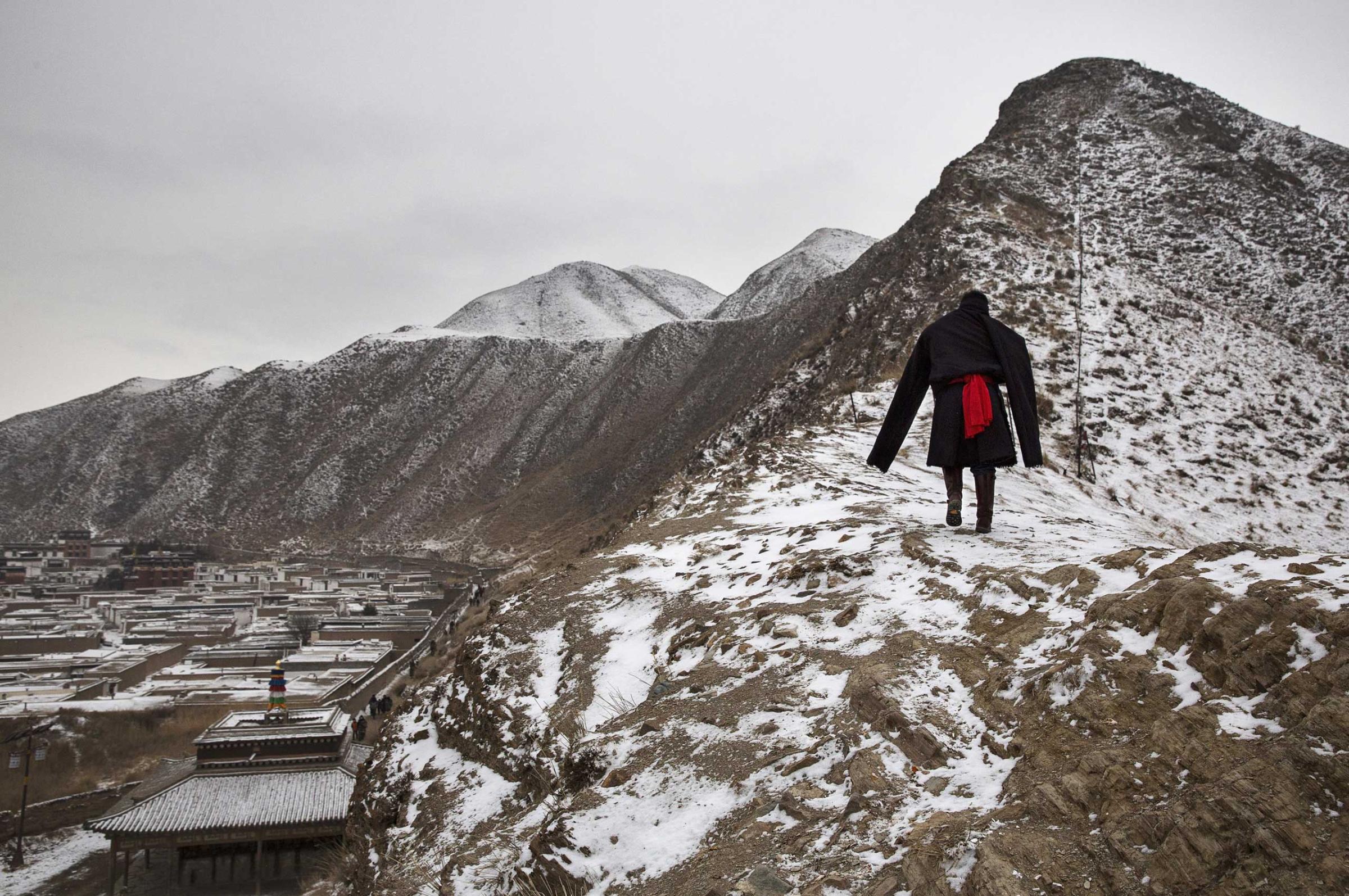 A Tibetan Buddhist man wears a traditional jacket as he walks on a hillside during Monlam or the Great Prayer rituals on March 4, 2015 overlooking the Labrang Monastery.