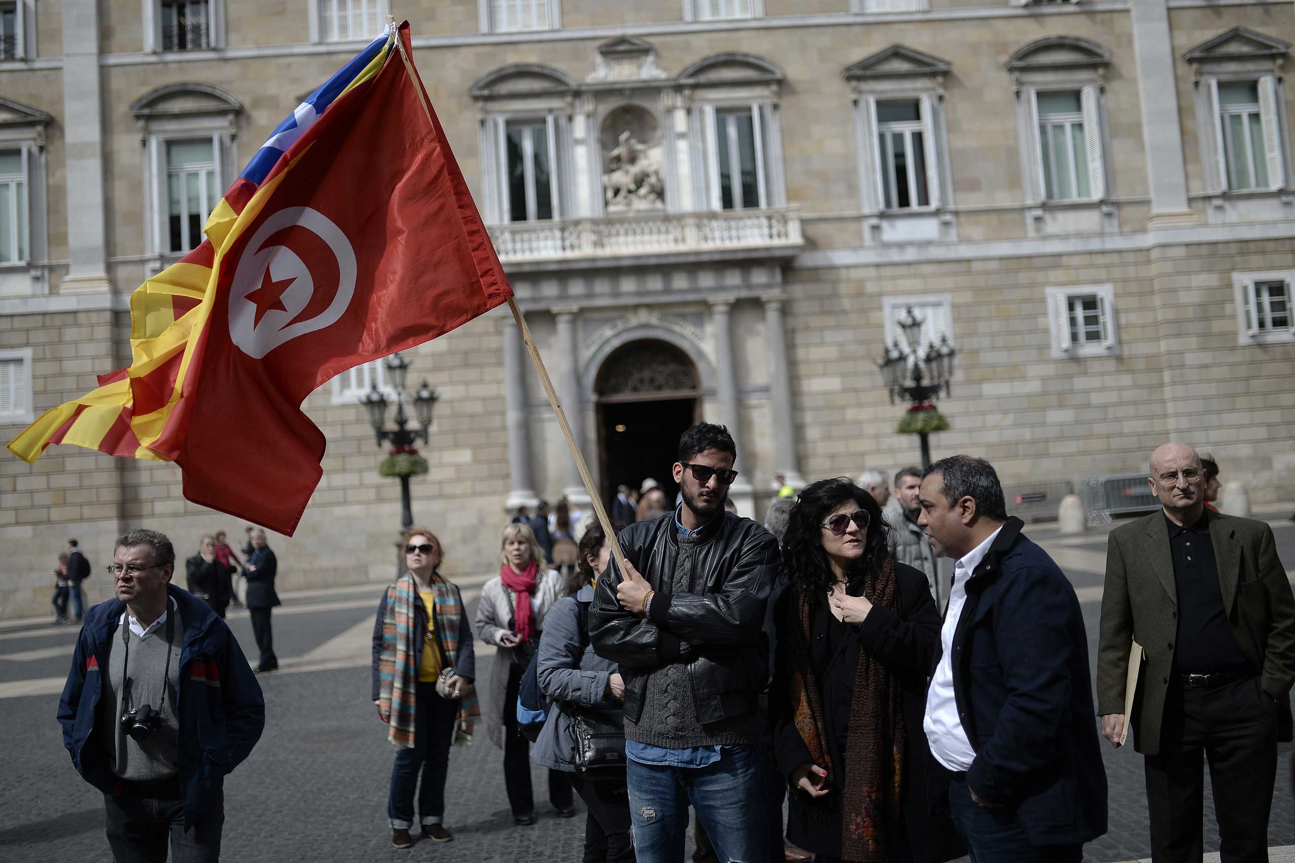 A man holds a Tunisian and a Catalan flag during a minute of silence held outside Barcelona's city hall in Barcelona on March 19, 2015.