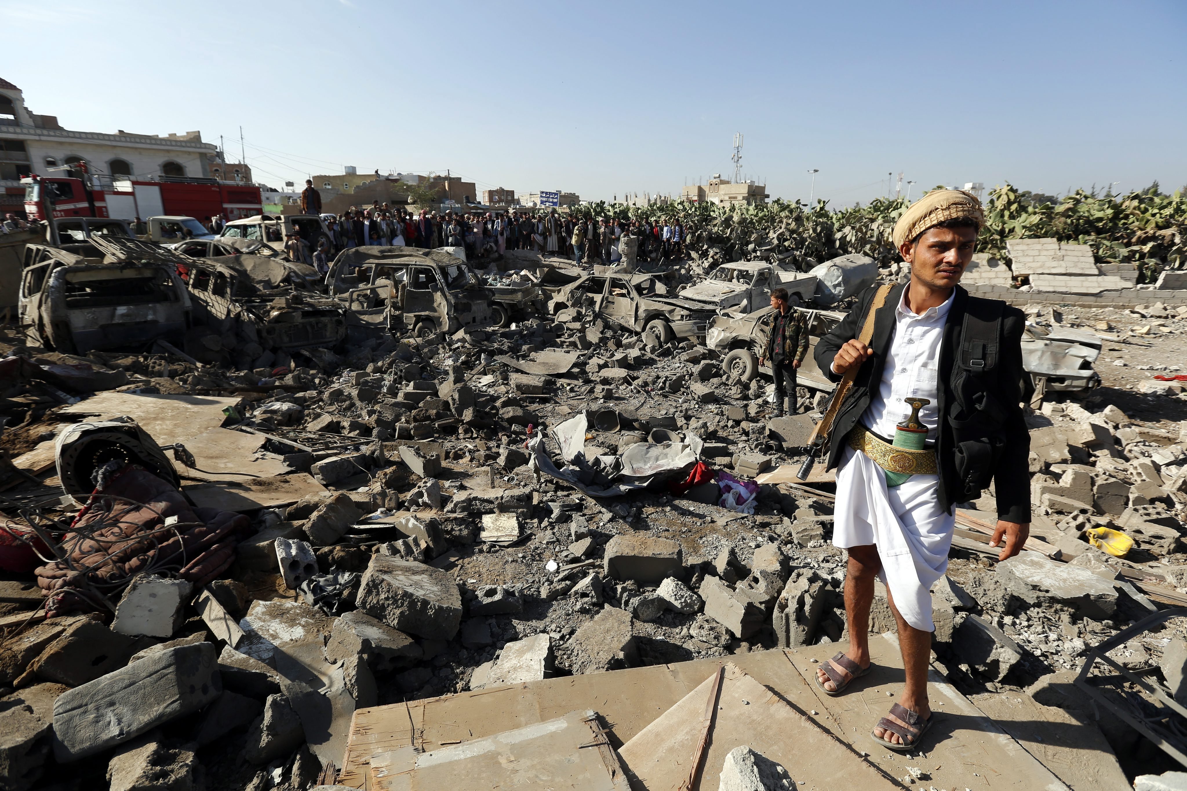 An armed member of Houthi militia (R) keeps watch as people gather beside vehicles which were allegedly destroyed by a Saudi air strike, in Sana'a, Yemen on March 26, 2015.