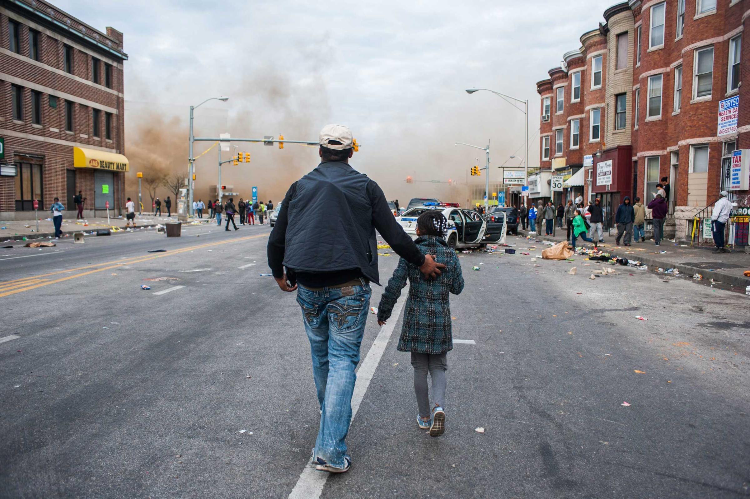 A man walks with his daughter along North Avenue toward a CVS that was set on fire during riots in Baltimore on April 28, 2015.