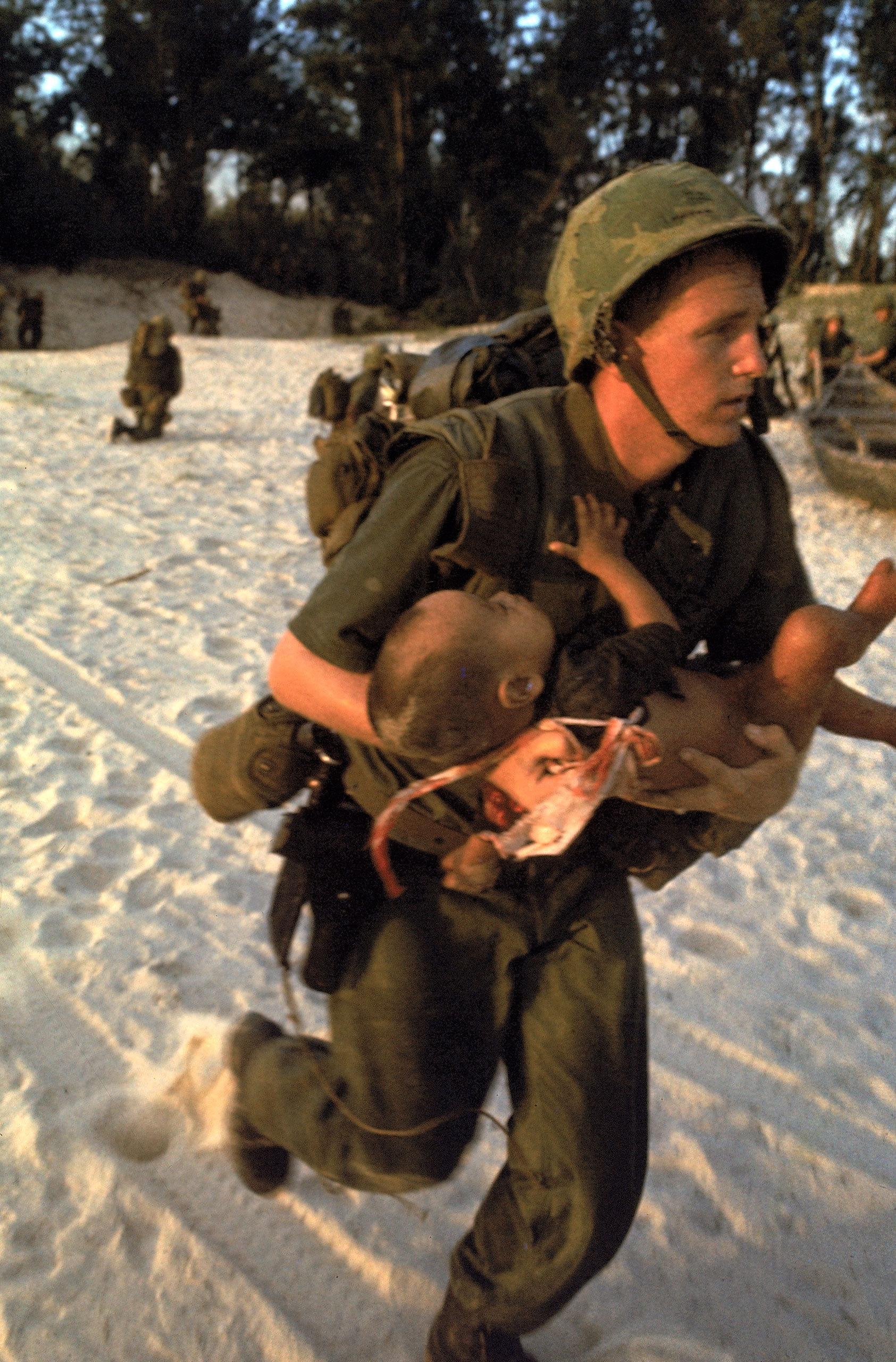 A corpsman attached to the Marines, who took the little boy from her, cradles him in his arms and double-times across the beach under heavy Vietcong sniper fire so he can treat the baby in safety.