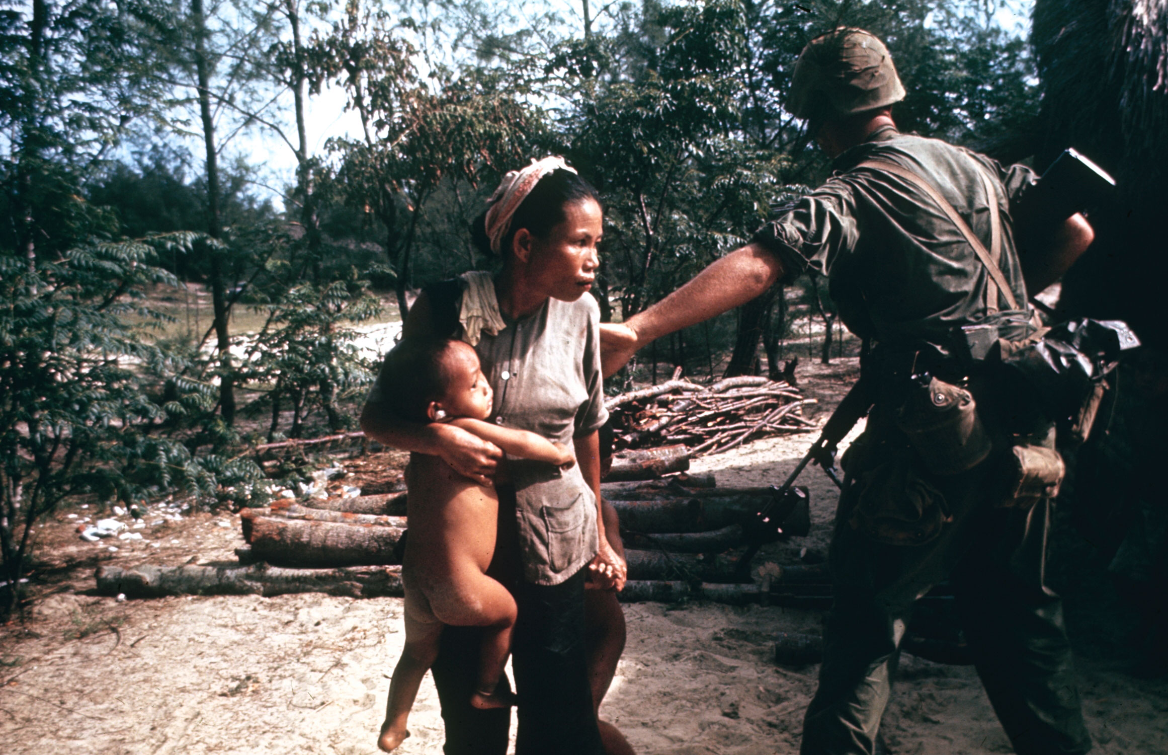 Marine leading a sweep into a fortified village pushes woman so he will have an unobstructed field of fire.