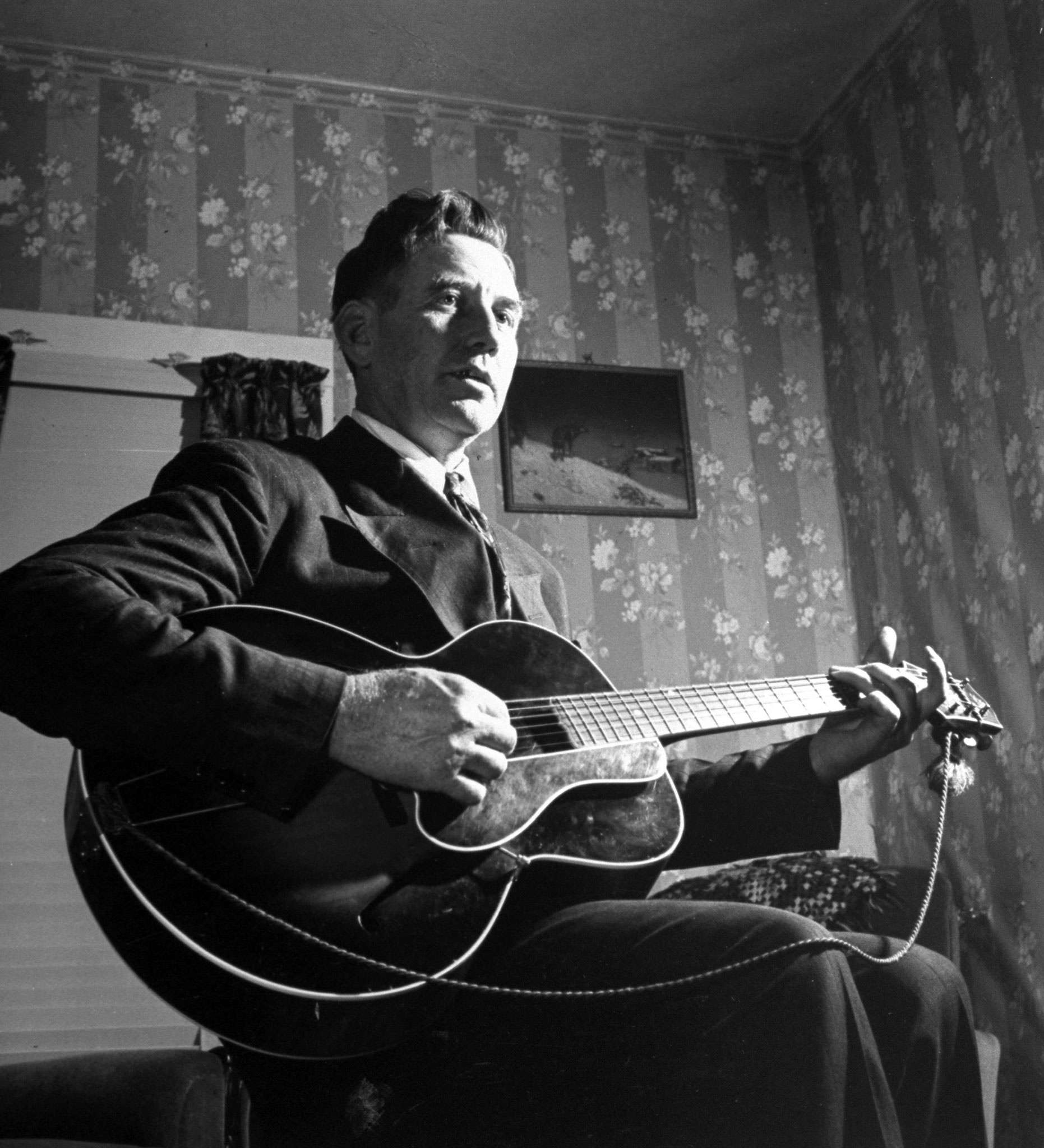 Considered the father of Country music, A. P. Carter, singing and playing guitar as he sits at home.