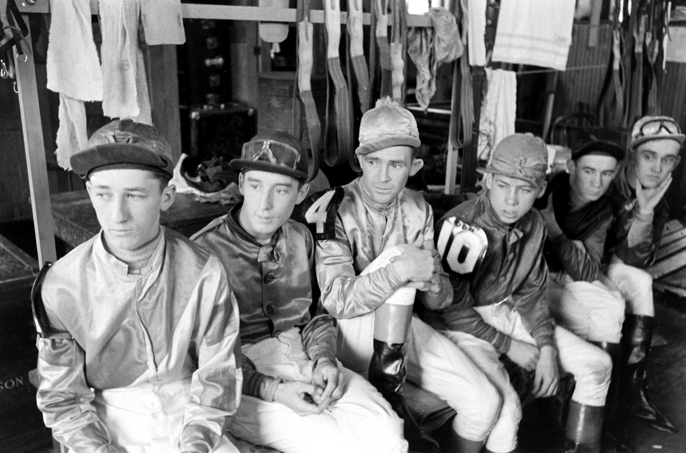 Churchill Downs jockeys in their quarters, include several who rode in the Kentucky Derby. At lower left is Hubert Leblanc who rode Miss Mary Hirsh's No Sir. Next to him is Hilton Dabson, who rode William Shea's and Miss E. G. Rand's Merry Maker. Fourth from left, with the number 10 on his sleeve is Basil James, who rode J. W. Parrish's Dellor.
