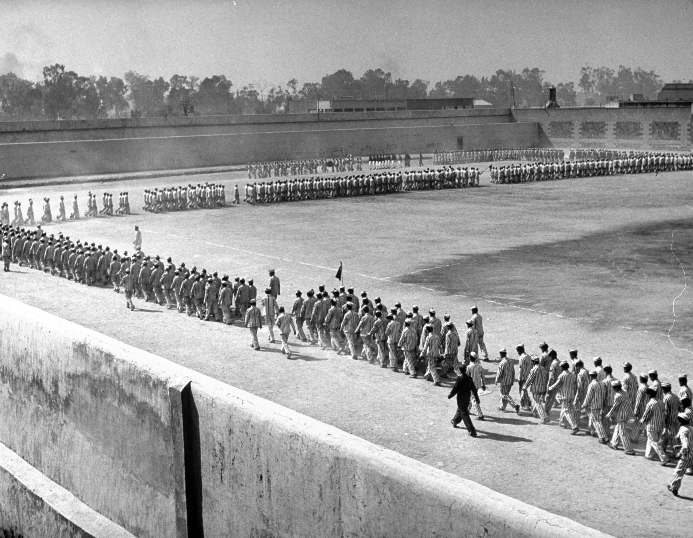 Prisoner parade moves smartly around the prison athletic field to band music. Army-style marching is part of new warden's program to improve morale.