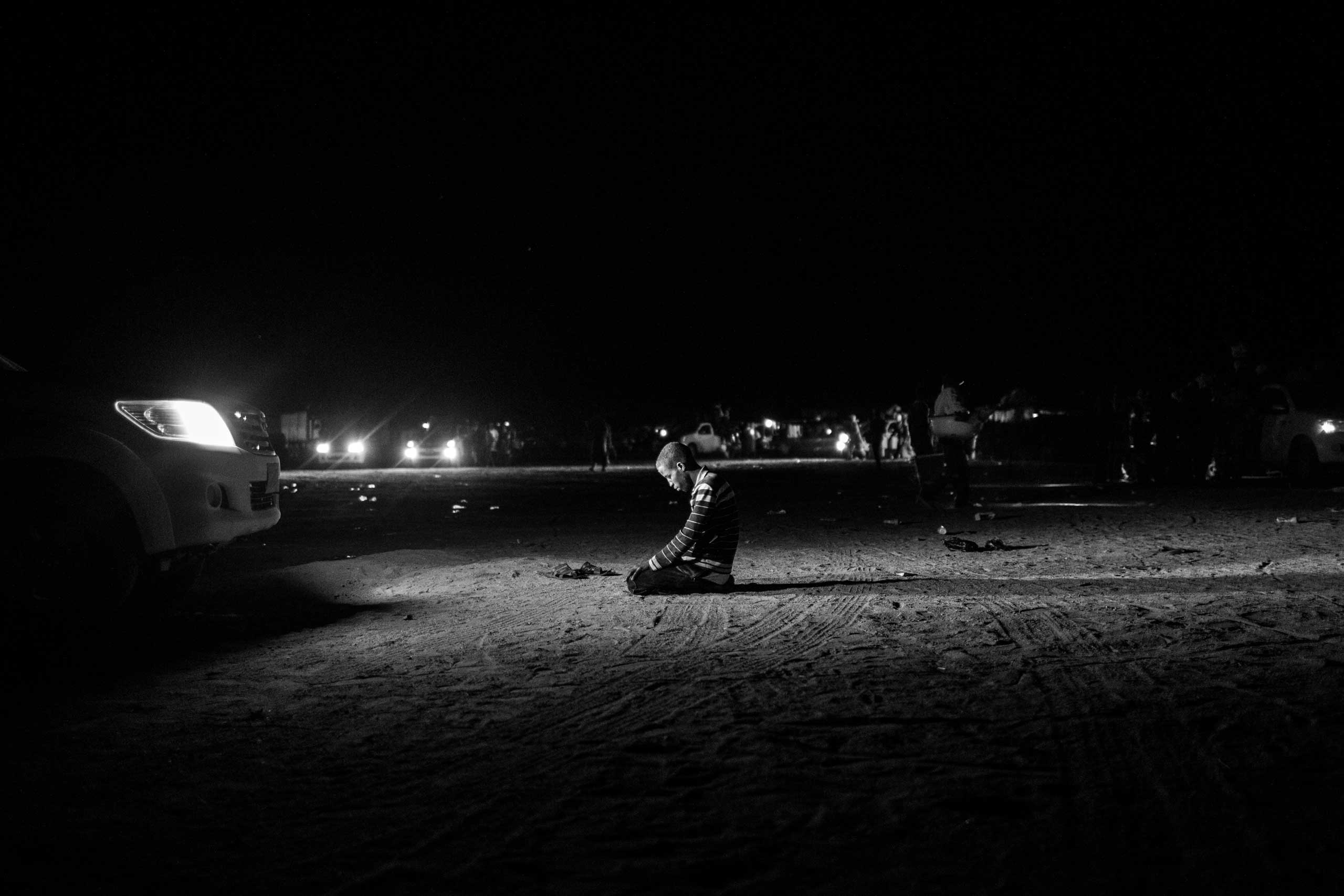 A migrant prays in the headlights of a pickup truck carrying him to Libya.