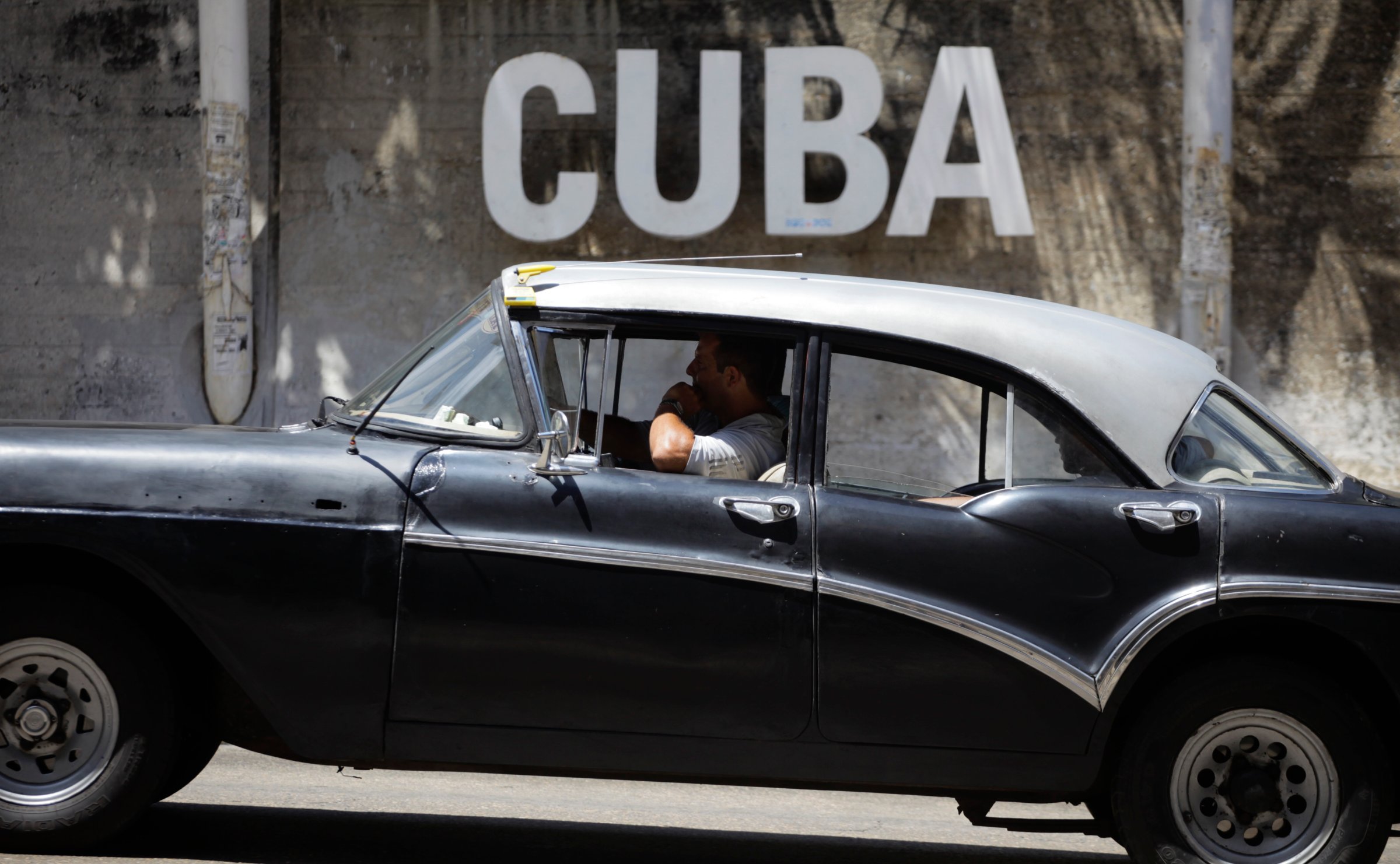 A man drives his taxi past a Cultural Center with the word "Cuba" on it, in Havana, Cuba,, April 14, 2015