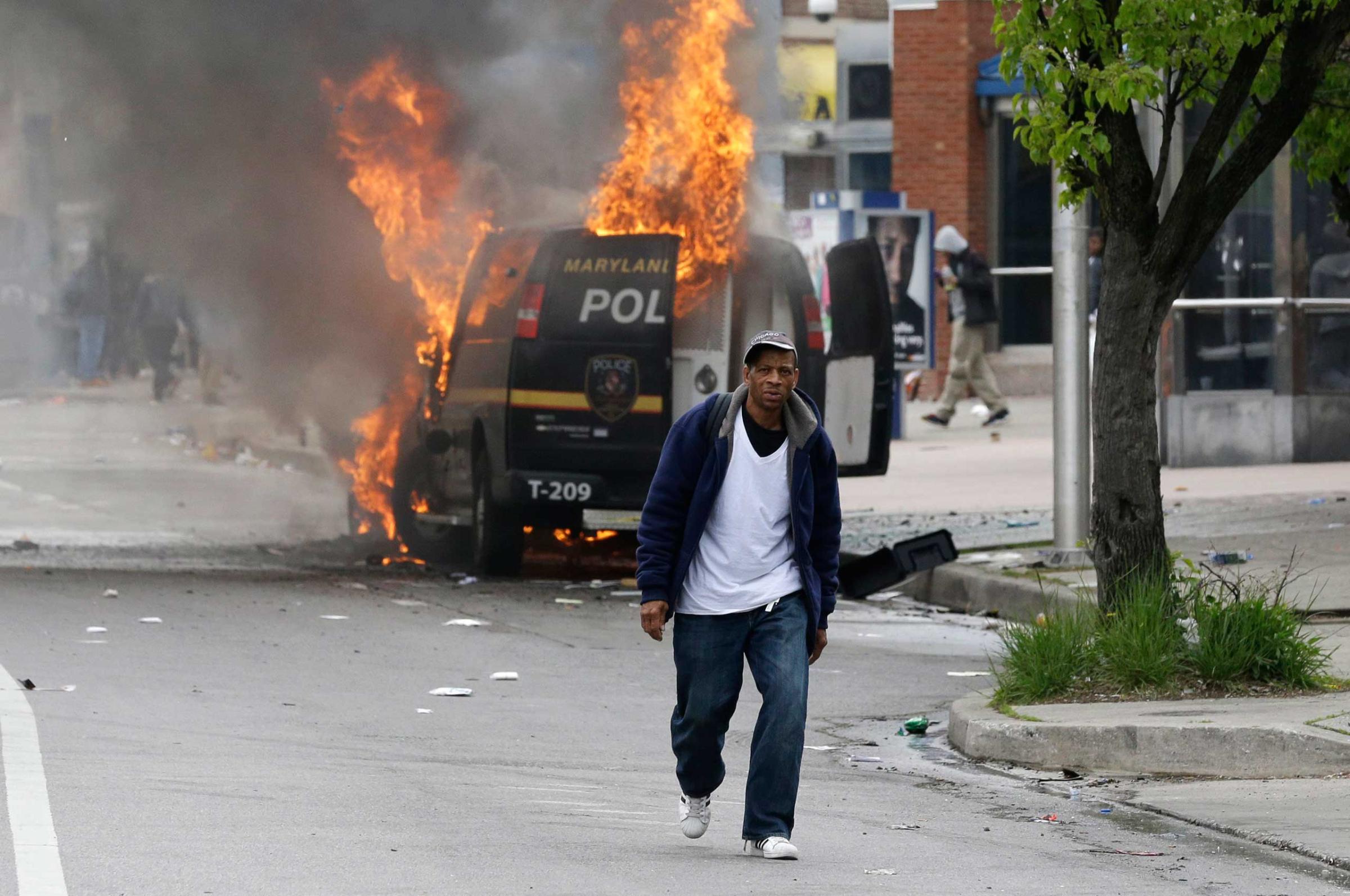 A man walks past a burning police vehicle in Baltimore on April 27, 2015.