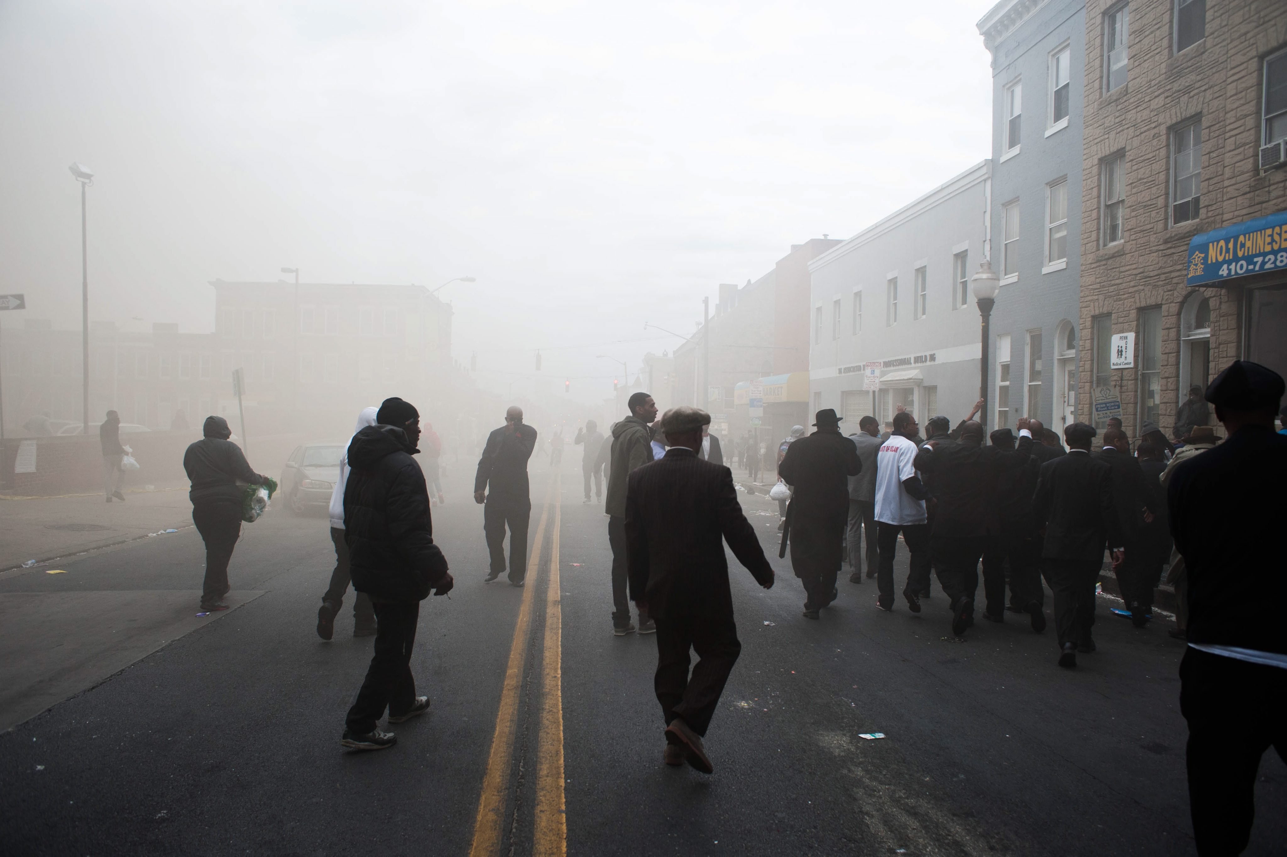 Protestors and pedestrians walk down Pennsylvania Avenue as smoke from a nearby CVS on fire covers the area in Baltimore on April 27, 2015.