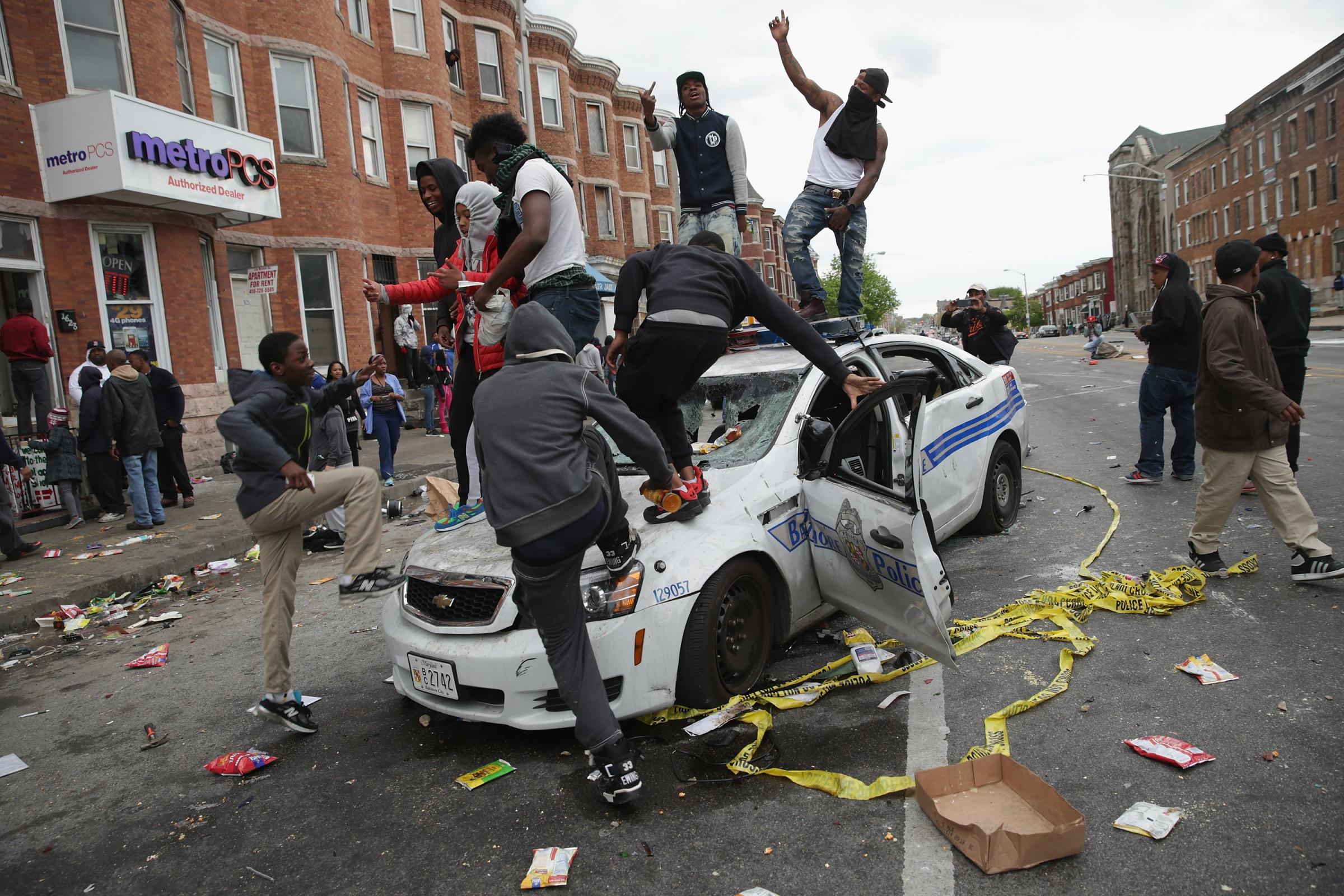 Demonstrators climb on a destroyed Baltimore Police car in the street near the corner of Pennsylvania and North avenues during violent protests following the funeral of Freddie Gray in Baltimore on April 27, 2015.