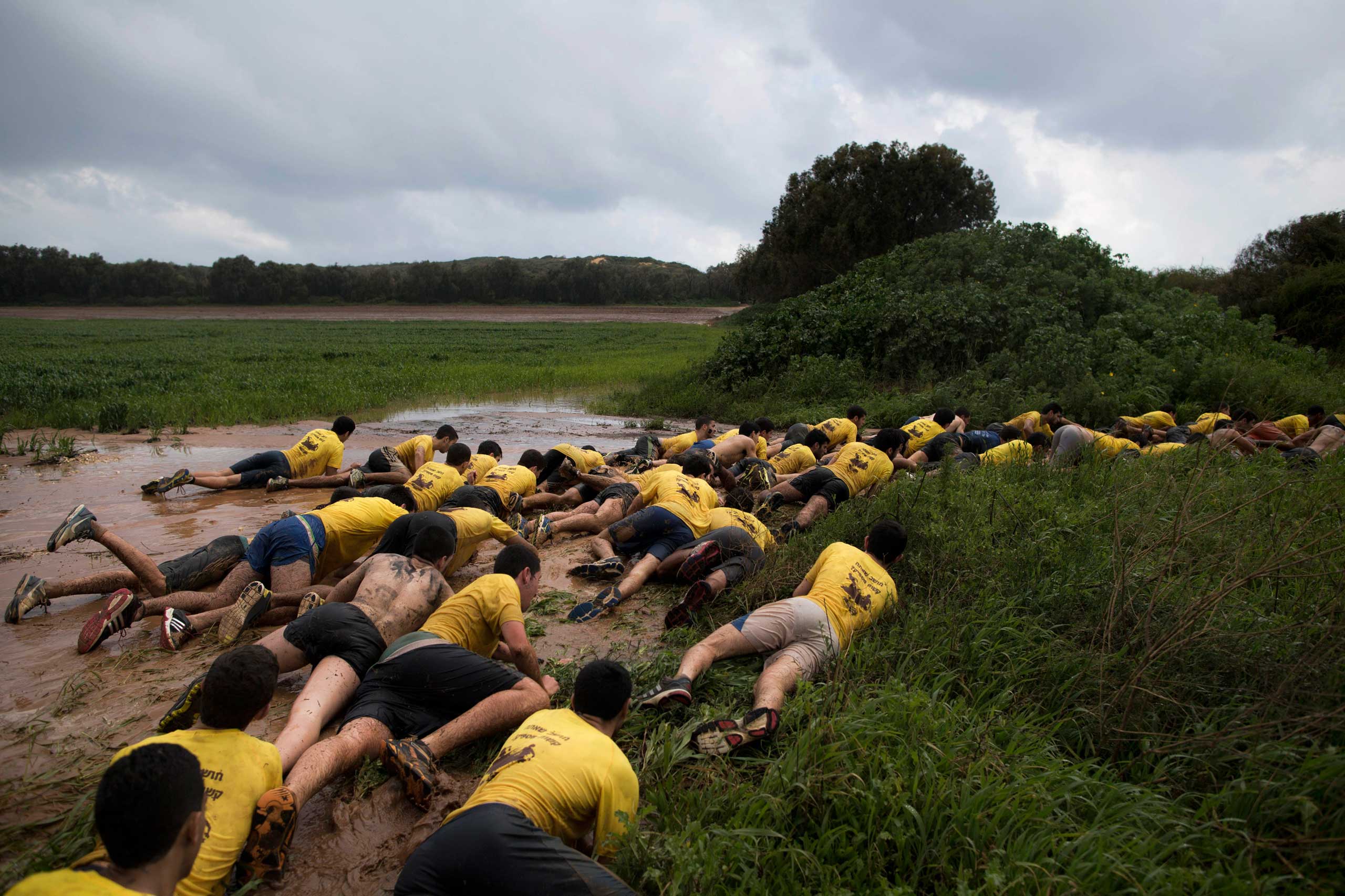High-school seniors preparing to join the Israeli military later this year crawl out of mud up to a grassy embankment during an exercise near Yakum, central Israel,  Feb. 13, 2015.