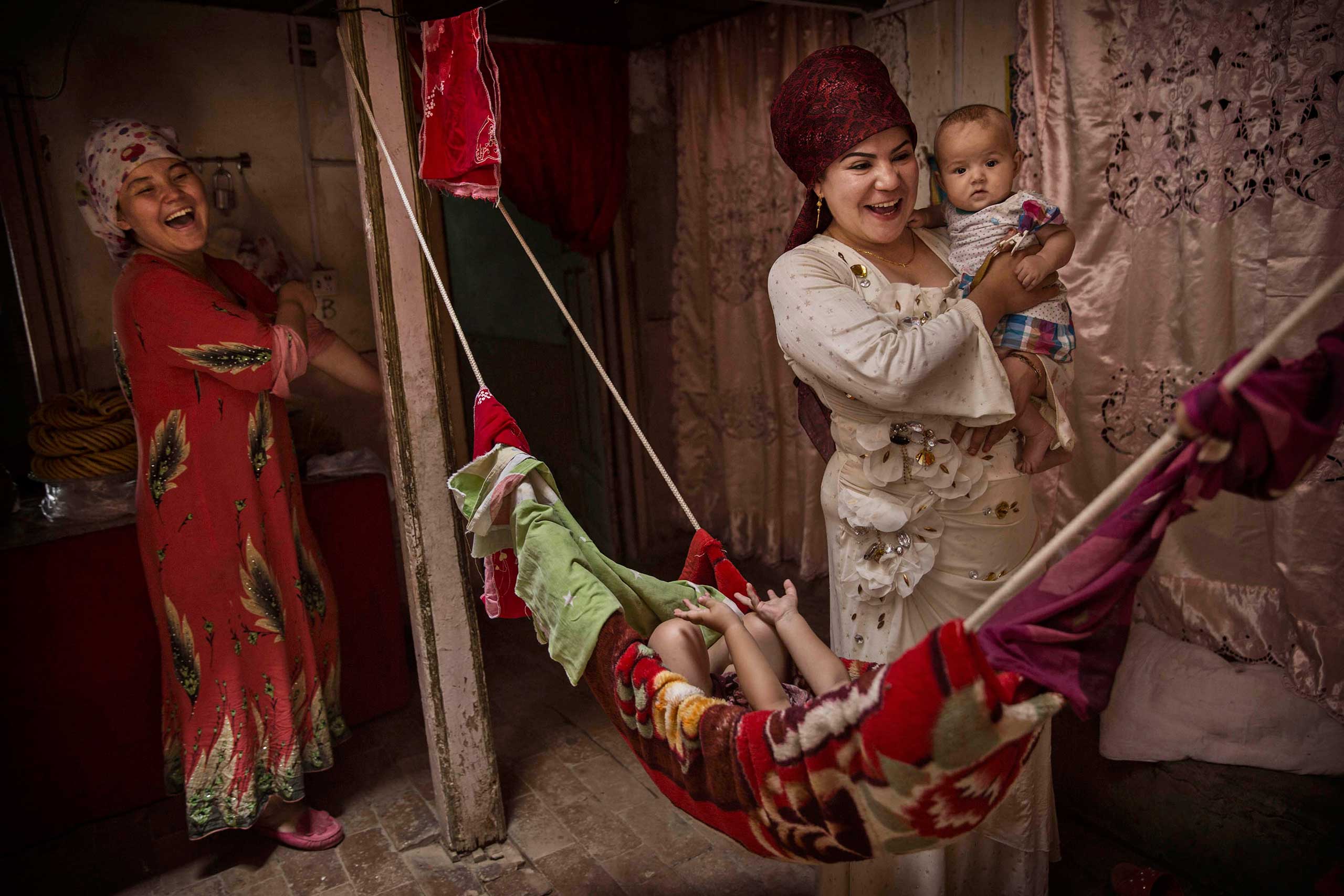Uighur women laugh as they take care of their children at home before the Eid holiday in old Kashgar, Xinjiang Province, China,  July 28, 2014.