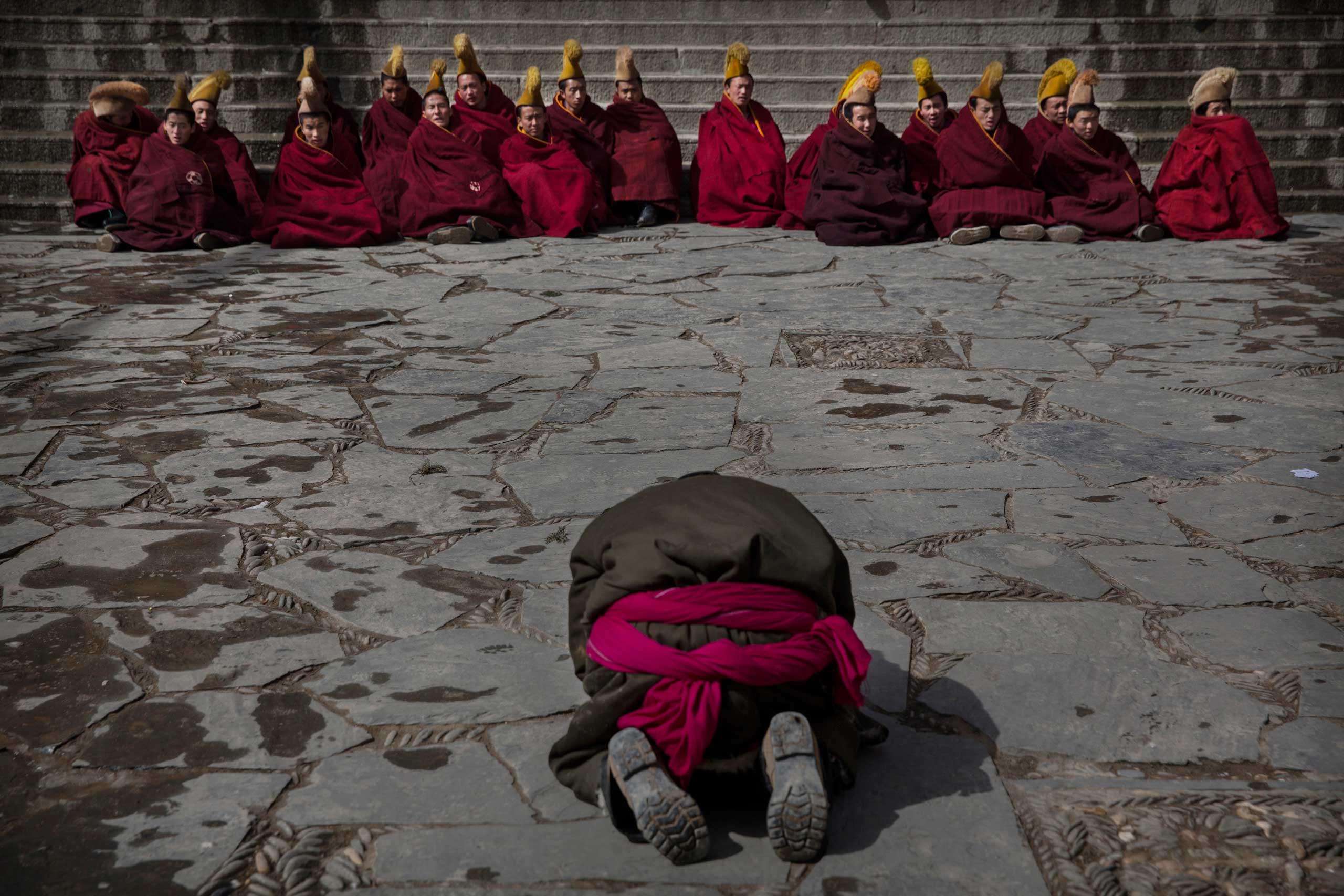 A Tibetan Buddhist man prays towards monks as they sit outside the main temple  during Monlam or the Great Prayer ritualsat the Labrang Monastery, Xiahe County, Amdo, Tibetan Autonomous Prefecture, Gansu Province, China, March 5, 2015.