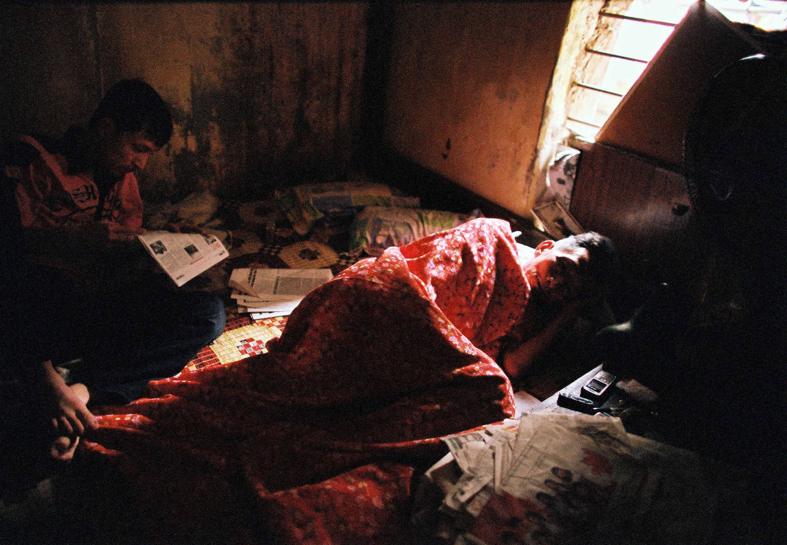An elderly man sleeps while his son reads newspaper in their tiny room in Hanoi, March 23, 2010.