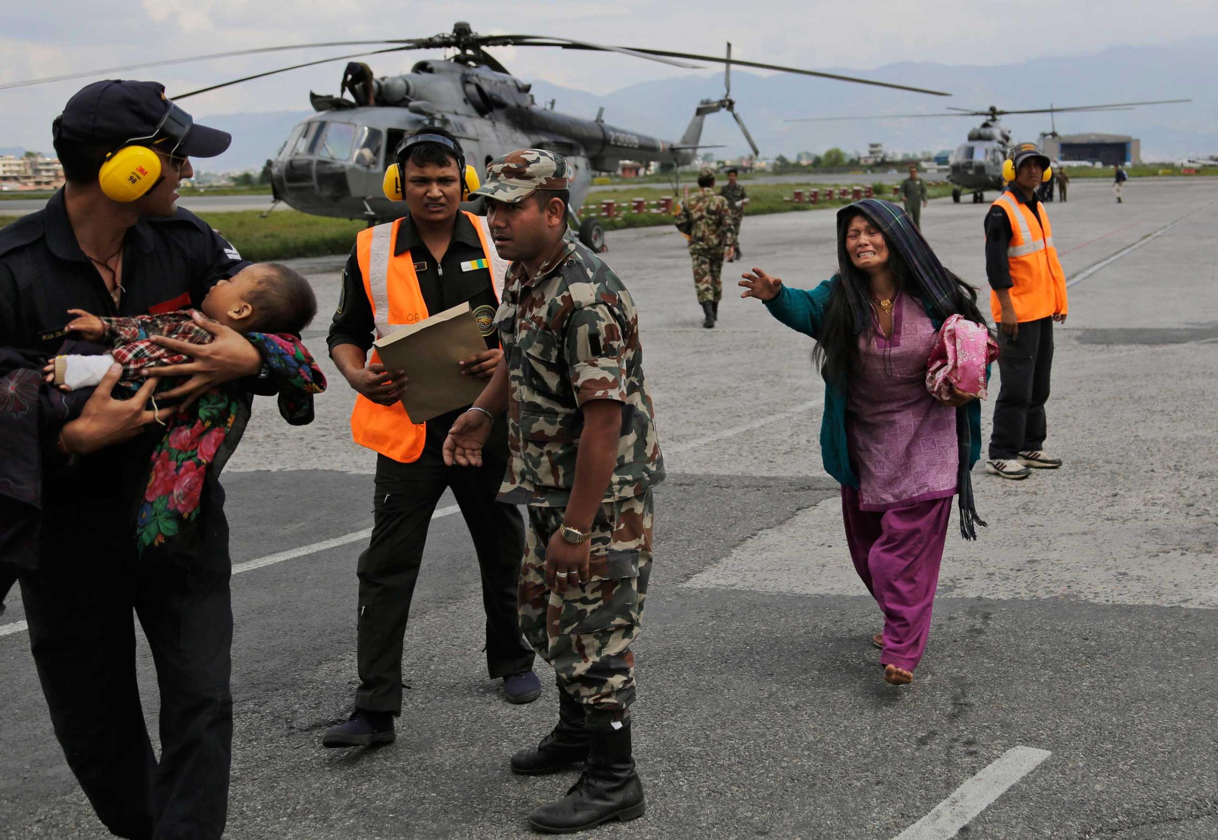 An Indian Air Force person walks carrying a Nepalese child, wounded in Saturday's earthquake, to a waiting ambulance as the mother rushes to join after they were evacuated from a remote area at the airport in Kathmandu on April 27, 2015.