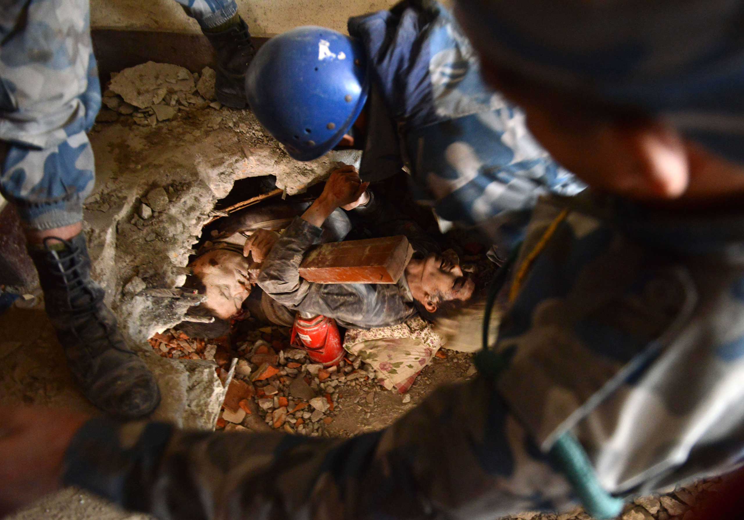 Nepalese rescue personnel help a trapped earthquake survivor, center right,  as his friend lies dead next to him in Swayambhu, in Kathmandu on April 26, 2015.