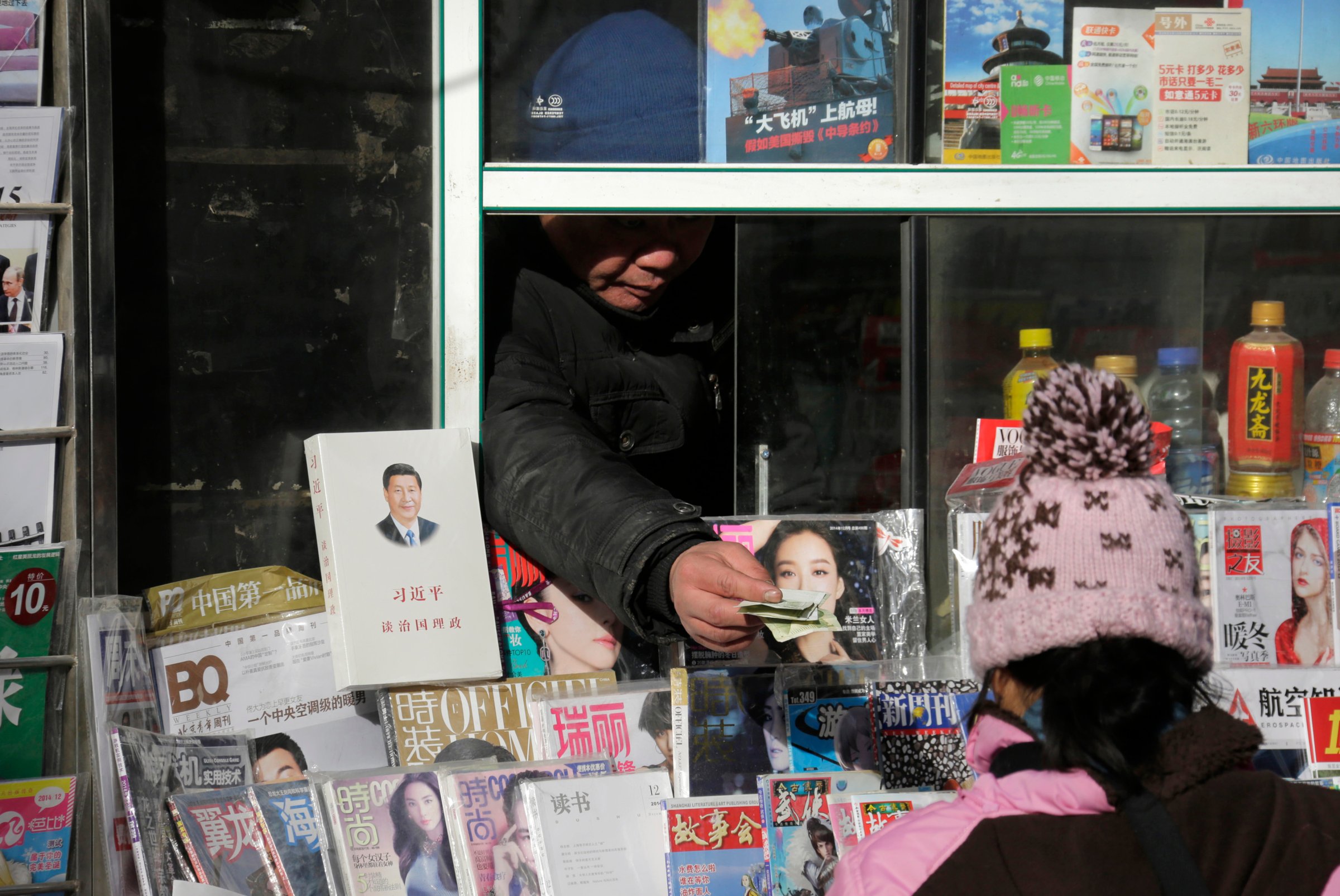 A newsstand vendor returns change to a customer near a book titled "Xi Jinping: The governance of China" displayed on sale in central Beijing