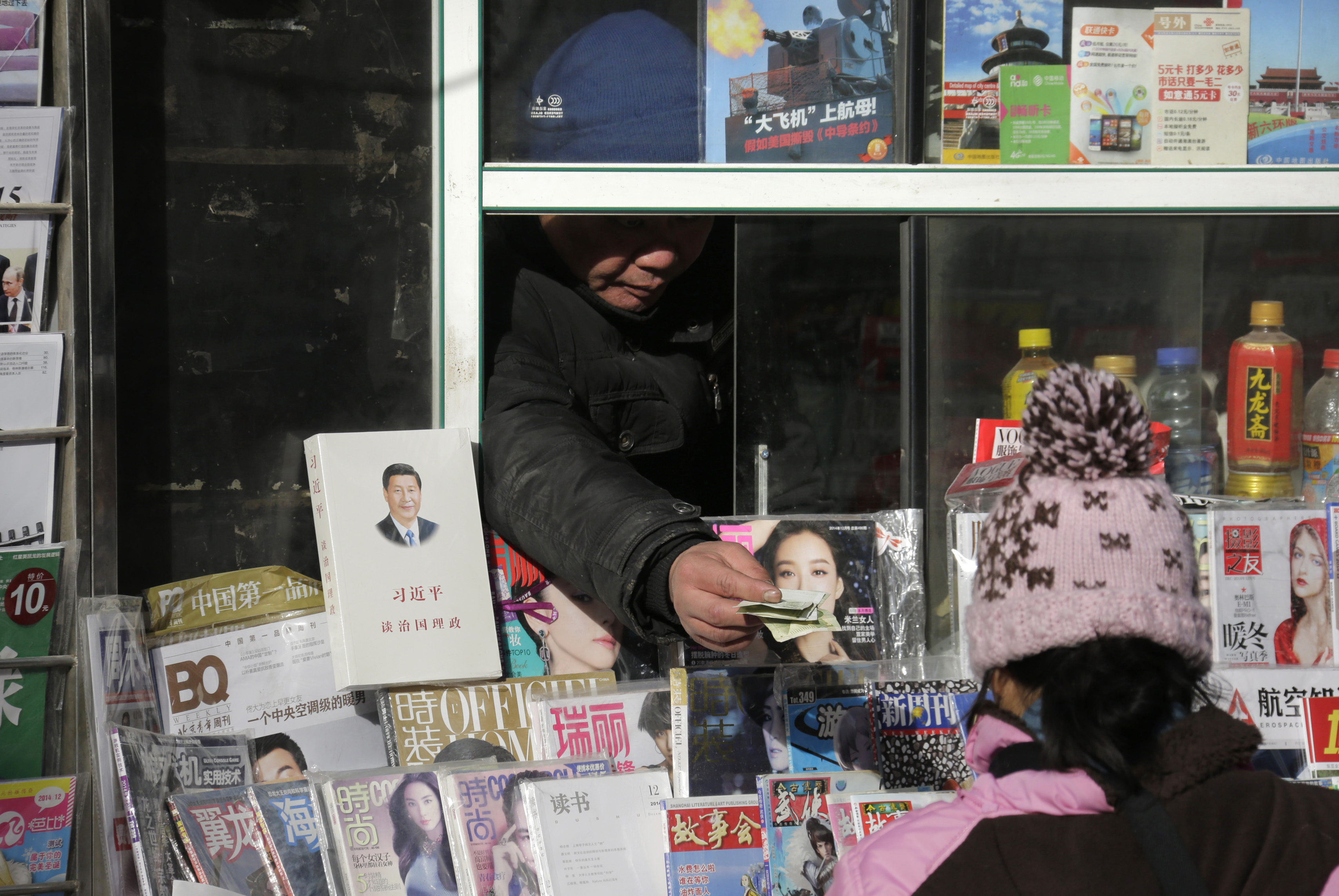 A newsstand vendor returns change to a customer near a book titled "Xi Jinping: The governance of China" displayed on sale in central Beijing