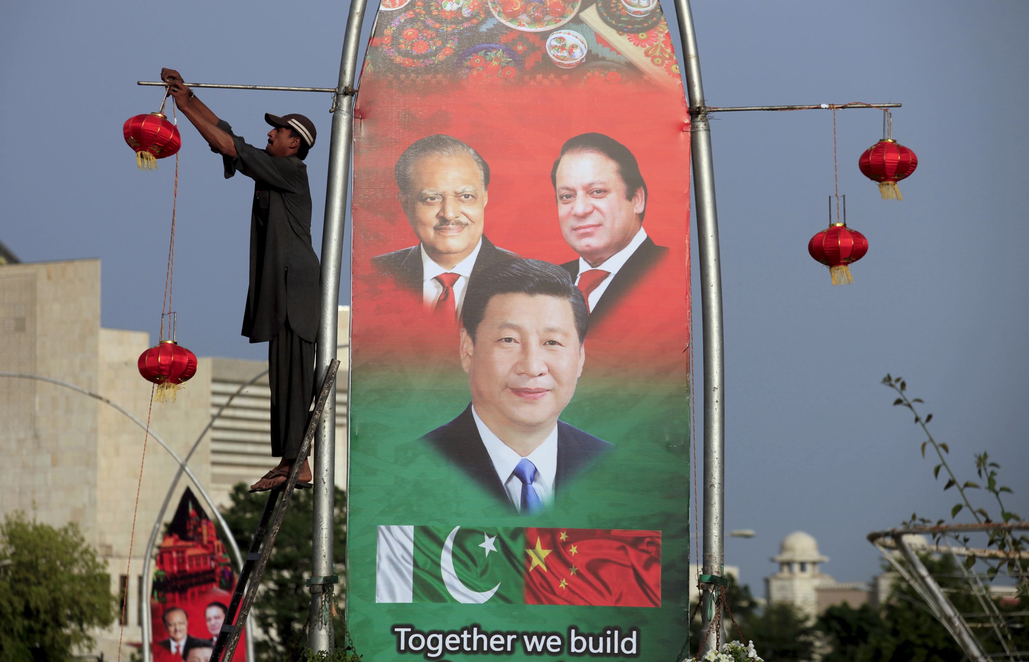 A man hangs decorations on a pole next to a banner showing Pakistan's President Hussain, China's President Xi and Pakistan's PM Sharif, ahead of Xi's visit to Islamabad