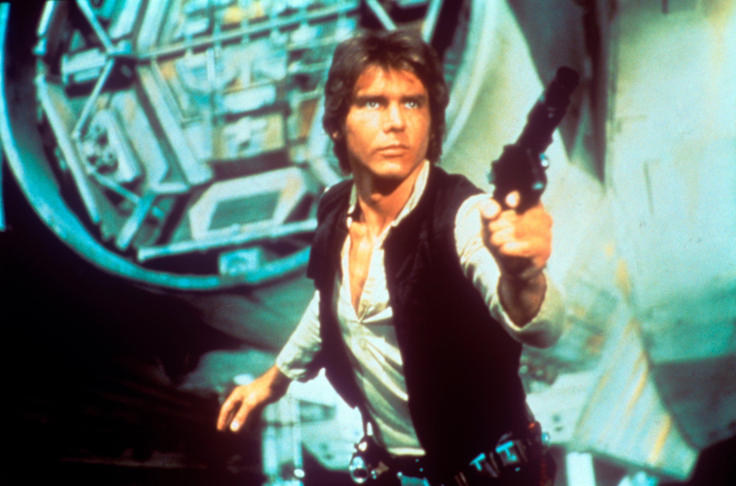 In a scene from George Lucas' epic space opera Star Wars, the American actor Harrison Ford as rebel smuggler Han Solo draws a gun against enemies; behind him can be seen a fantastic space shuttle. USA, 1977.