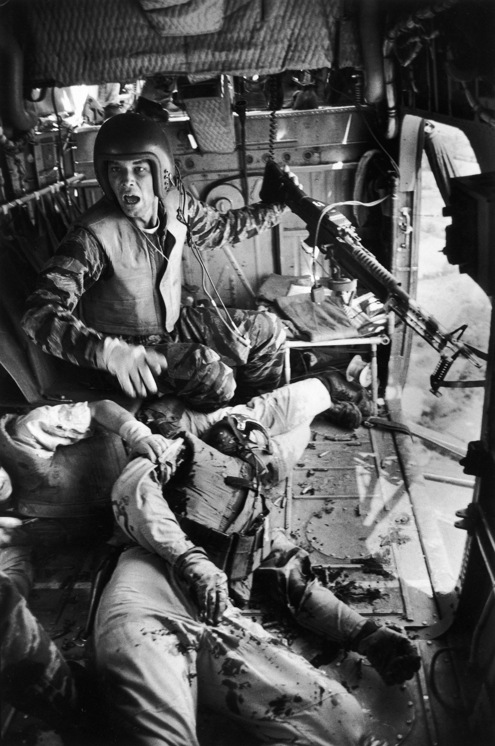 A mortally wounded comrade at his feet, Lance Cpl. James C. Farley, helicopter crew chief, yells to his pilot after a firefight in Vietnam, 1965.