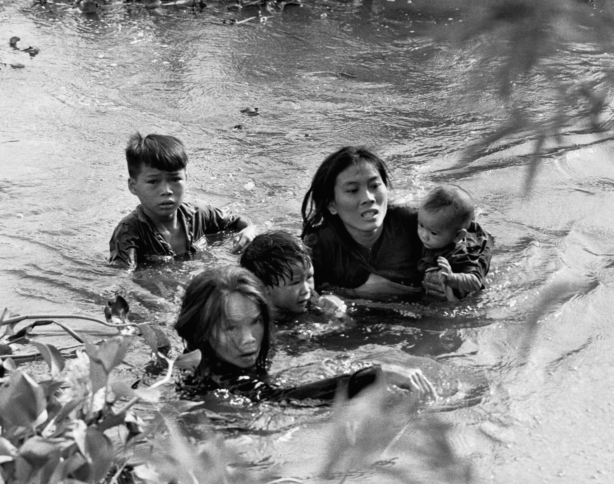 A Vietnamese mother and her children wade across a river, fleeing a bombing raid on Qui Nhon by United States aircraft on Sept. 7, 1965.