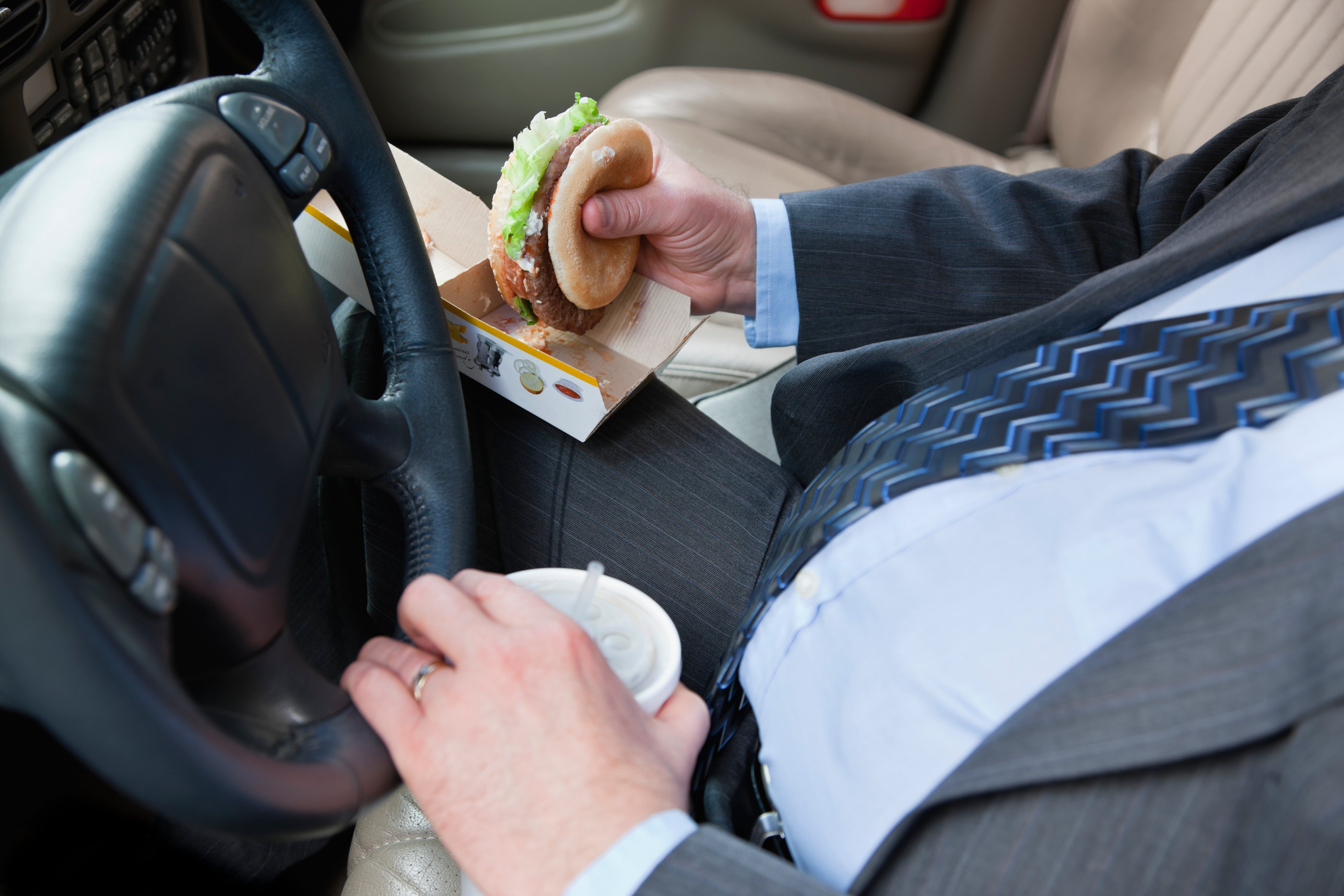 man driving a car, eating a burger