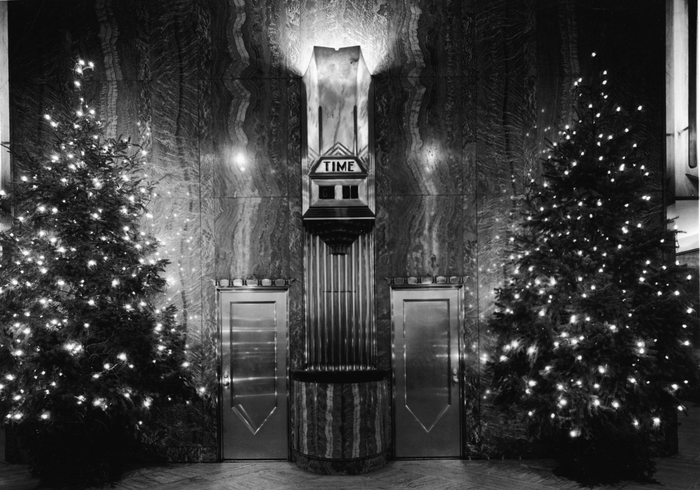 The lobby of the Chrysler Building (1930, William van Alen, architect) and its clock, two doors, and two Christmas trees with strings of light, the wall is red Moroccan marble, New York, mid 20th Century.