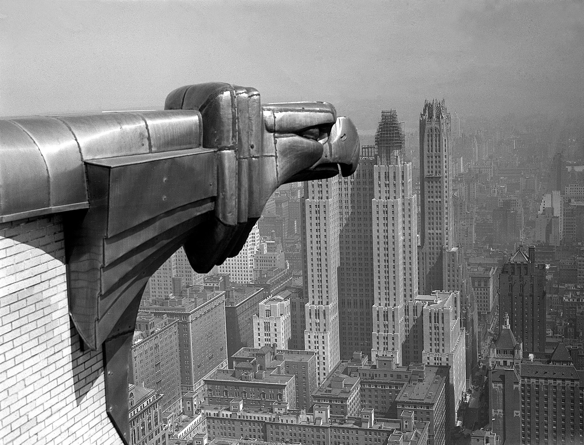 A gargoyle atop the Chrysler Building watches vigilantly over the rising Gotham towers of midtown Manhattan.
