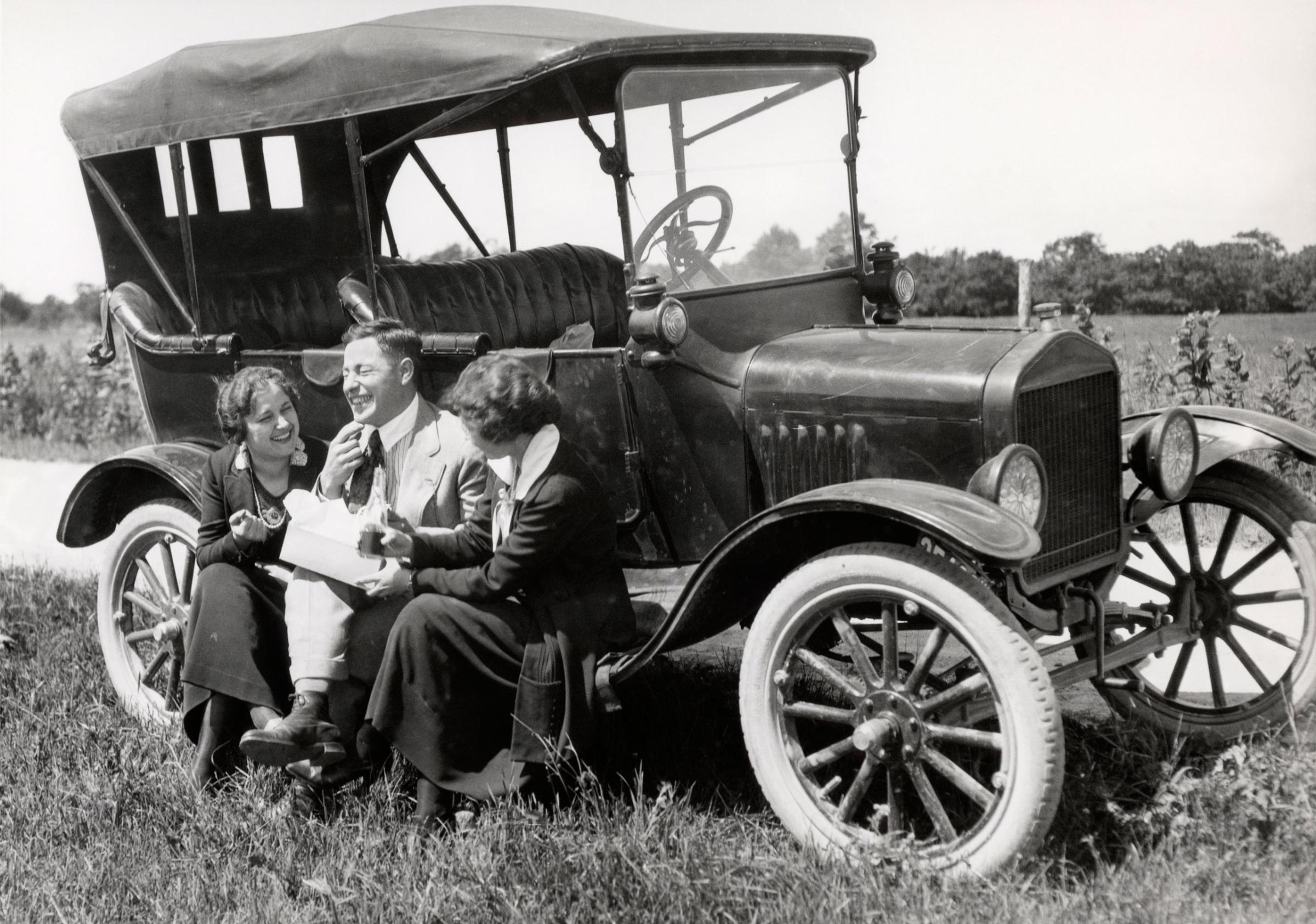 Two Women and One Man Sitting On Running Board Of Model T Ford Eating Lunch, 1920.