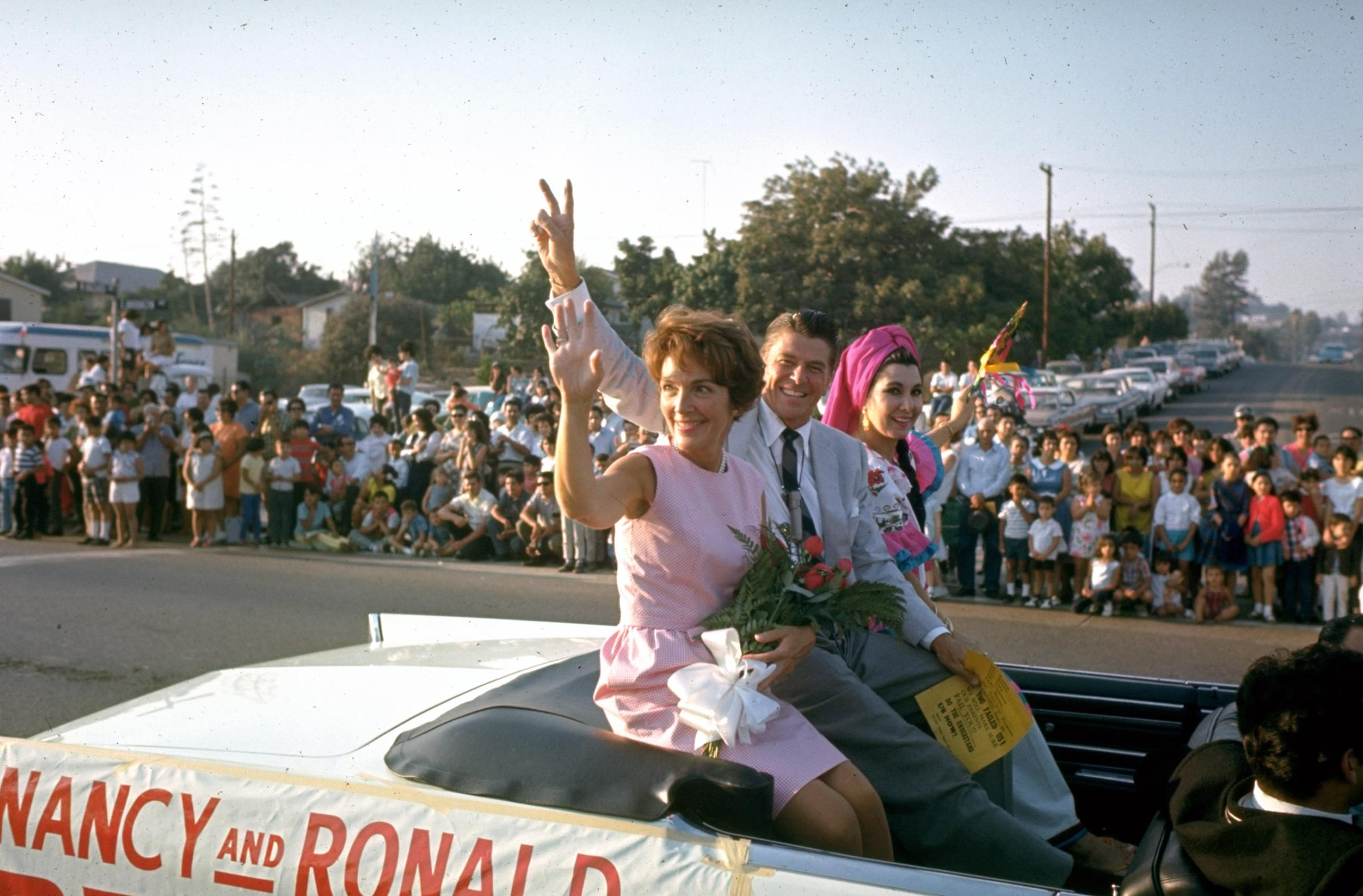 California Republican gubernatorial candidate Ronald Reagan,wife Nancy waving to spectators as they ride in back of convertible car outside while on the campaign trail, 1966.