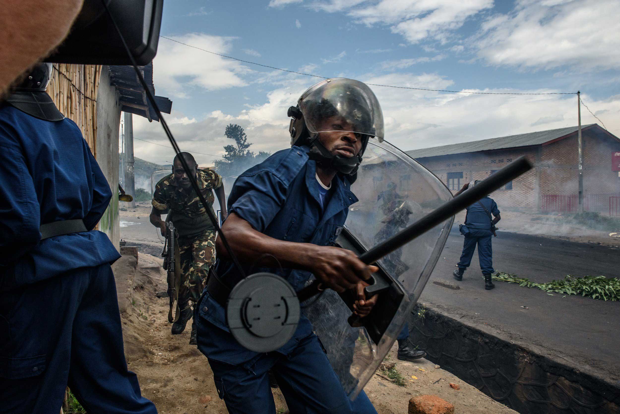 A police officer holding a baton and army forces run after protesters throwing stones during a demonstration against incumbent President Pierre Nkurunziza's bid for a third term in Bujumbura, Burundi, on May 13, 2015.